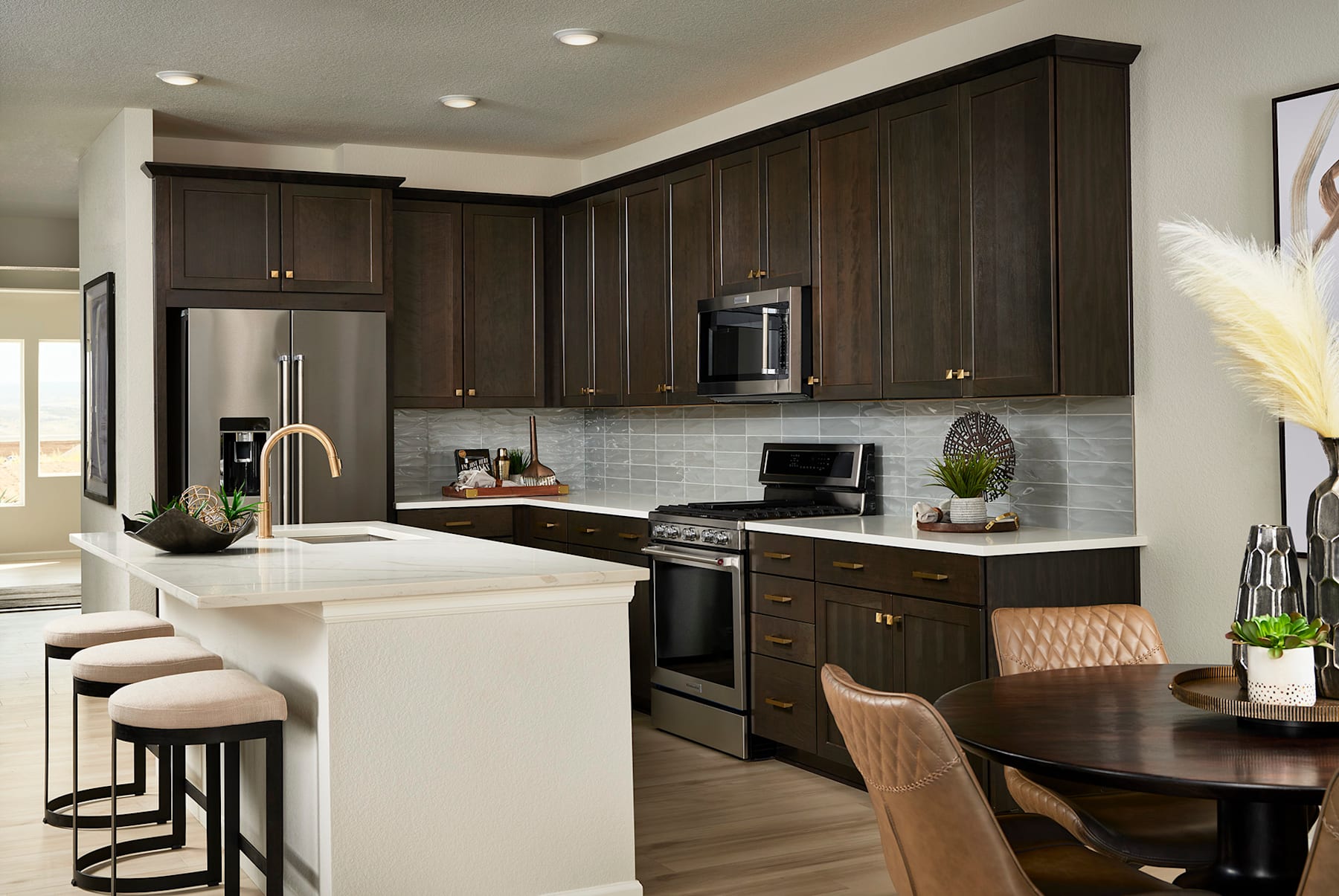 A modern and well-equipped kitchen with dark wood cabinets, stainless steel appliances, and a white countertop with a dining area in the background.