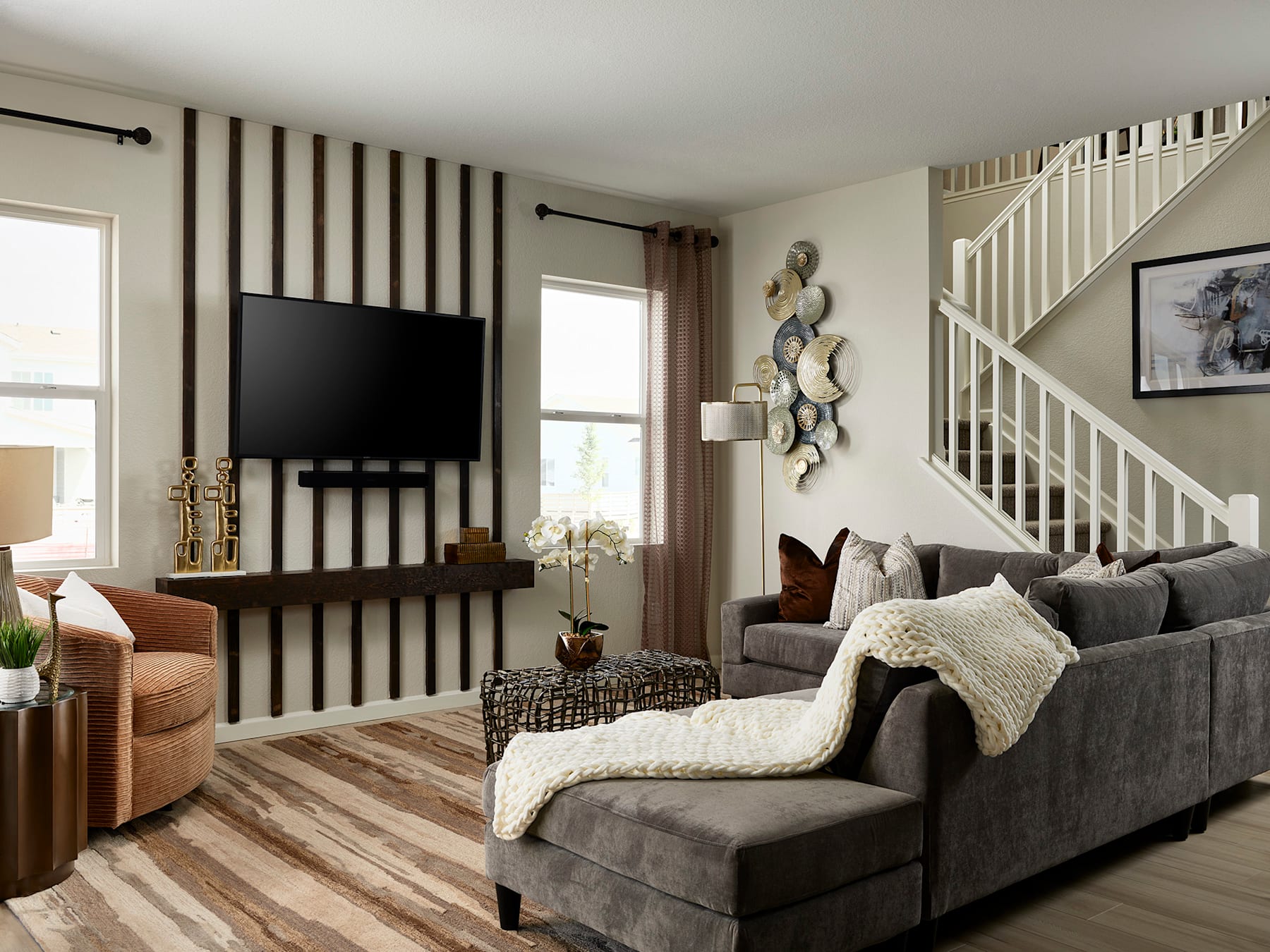 A cozy and inviting living room with a large gray sectional sofa, a TV mounted on the wall, and various decorative elements such as wall art and a potted plant.