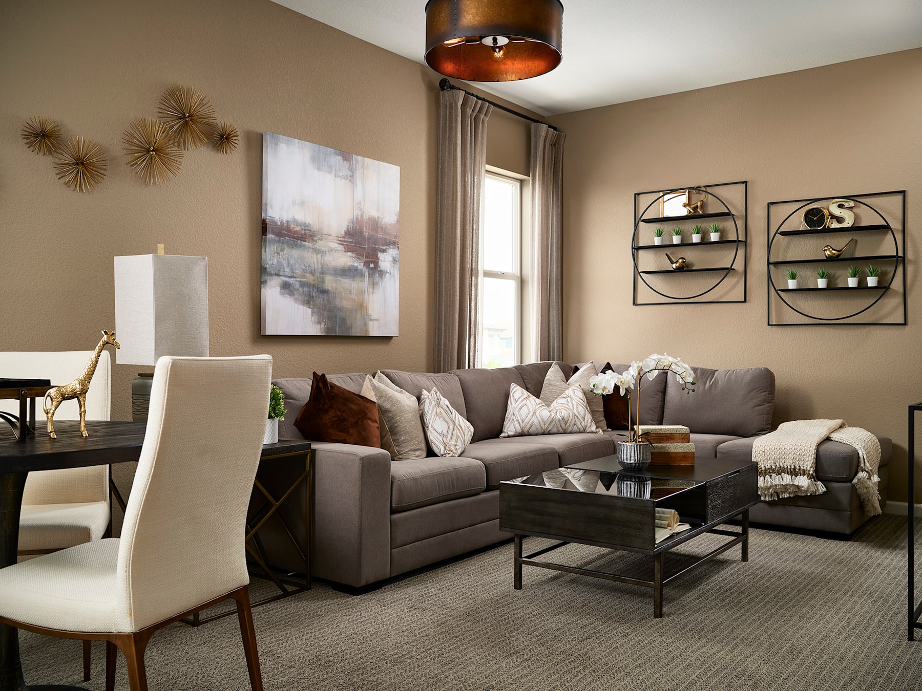 A cozy and inviting living room with a gray sectional sofa, a glass-topped coffee table, and various decorative elements such as wall art, shelves, and a pendant light fixture.