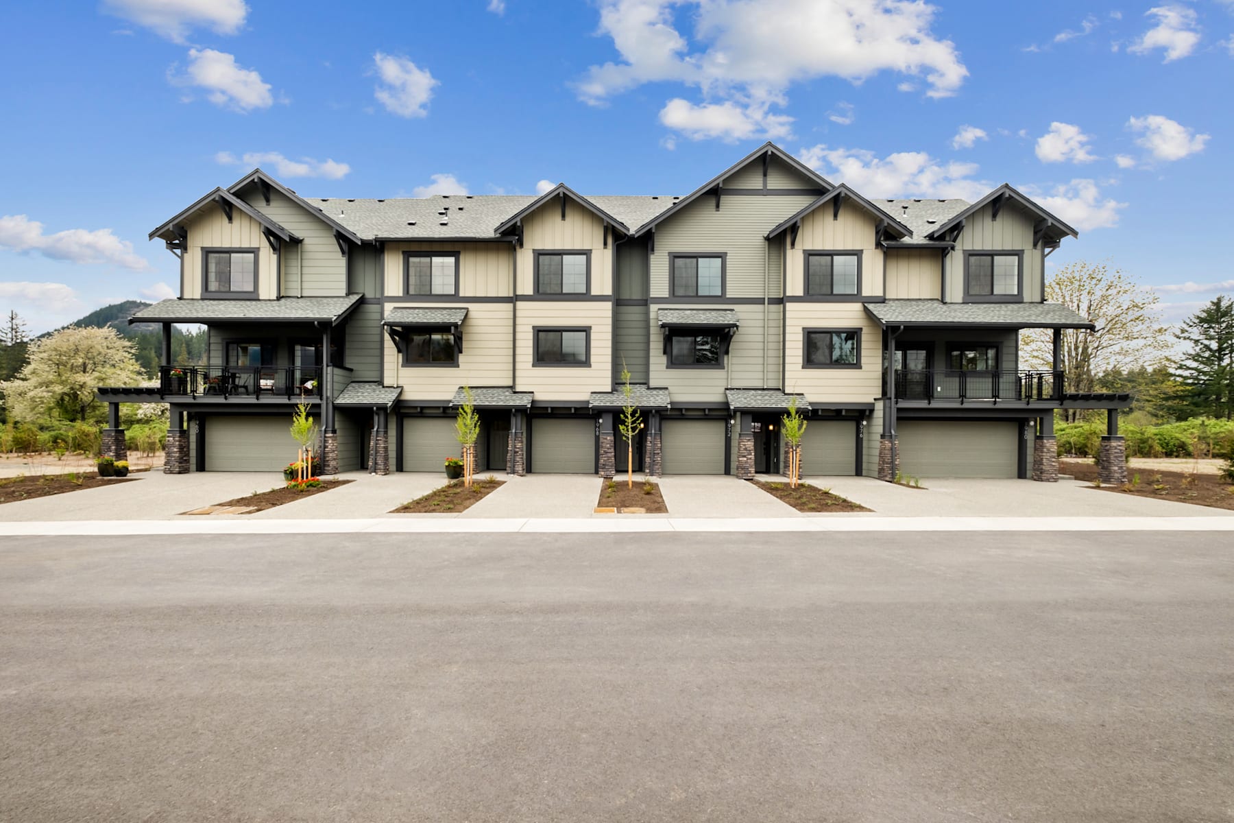 A row of modern, multi-story townhouses with gabled roofs and attached garages, set against a backdrop of cloudy blue skies.