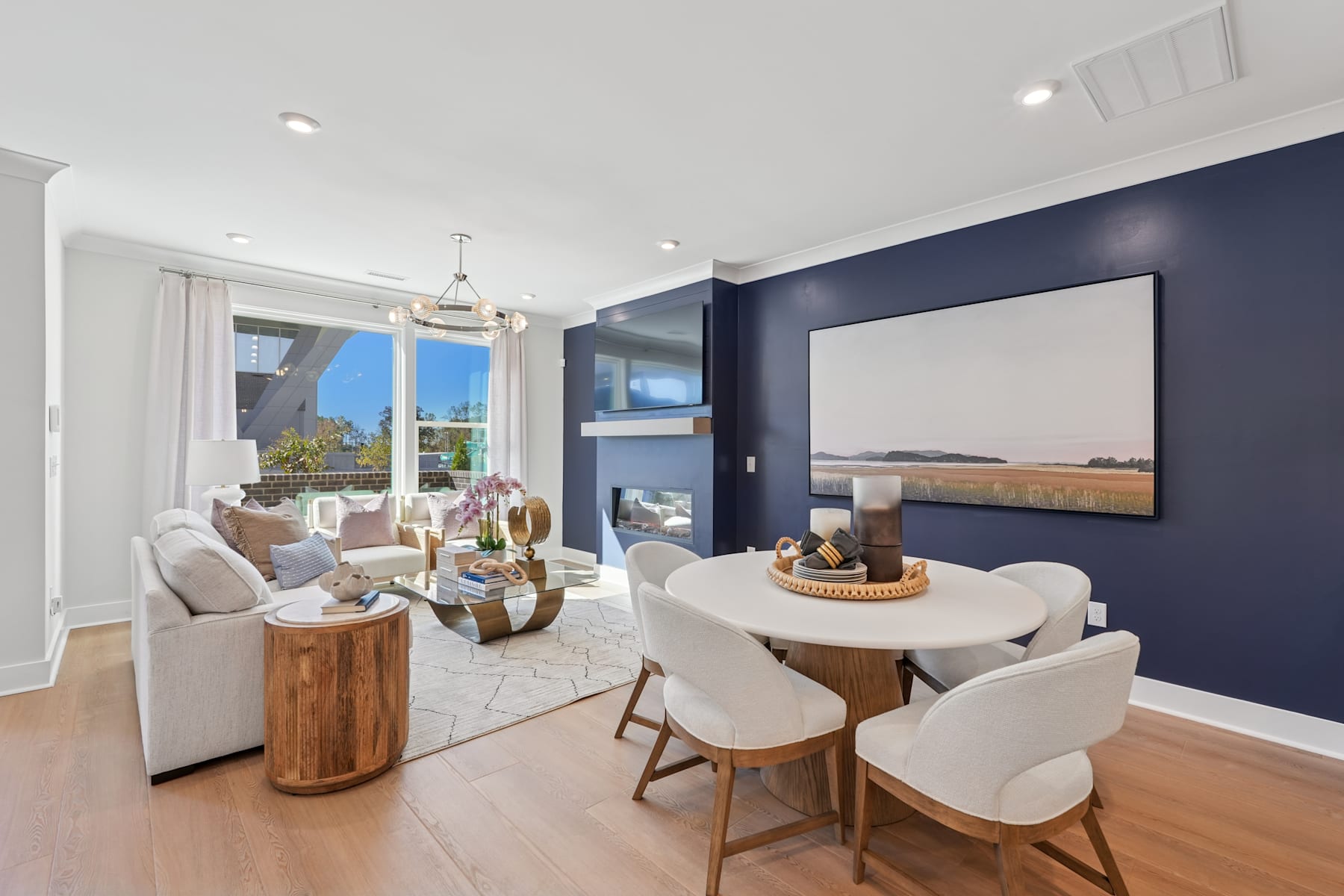 A modern and stylish living room with a dining area, featuring a large TV on the wall, comfortable white chairs, and a wooden table with decorative elements.