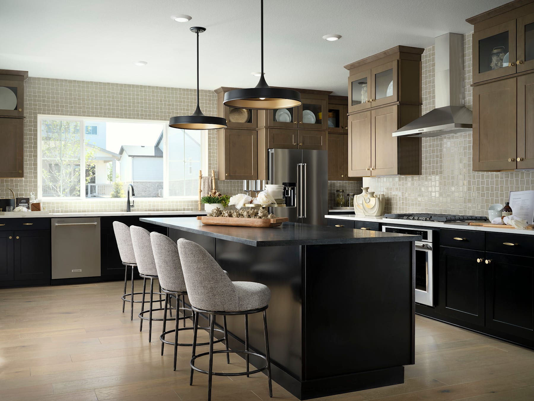 A modern and spacious kitchen with a large central island, dark cabinets, and pendant lighting fixtures, set against a backdrop of light-colored walls and tile flooring.