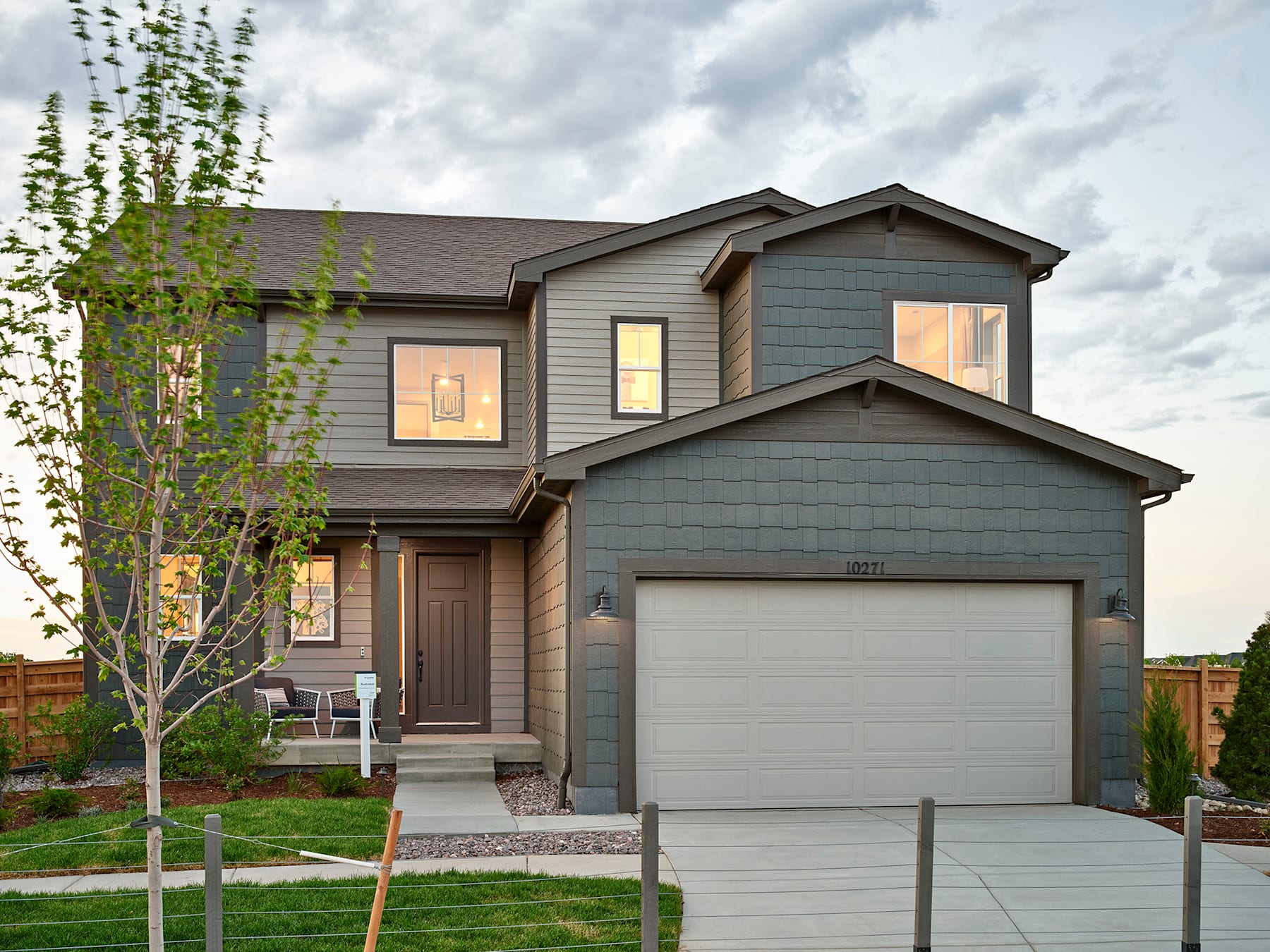 A two-story residential house with a garage, surrounded by a grassy yard and trees in the background.
