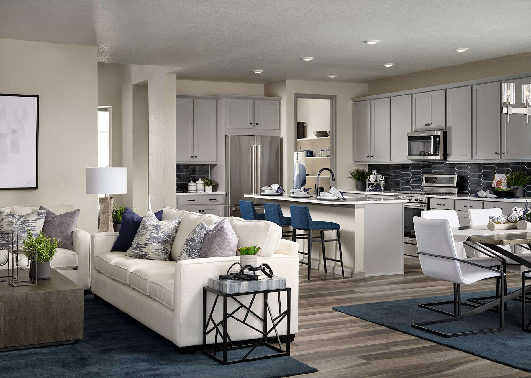 A modern and spacious open-concept living room and kitchen area with white cabinets, stainless steel appliances, and a comfortable white sofa with decorative pillows.