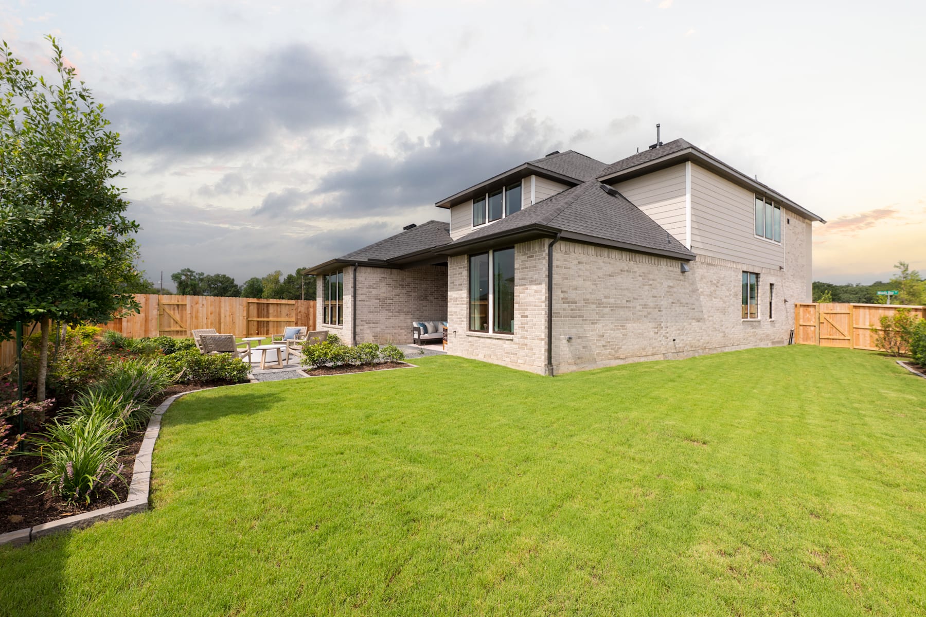 A modern two-story house with a well-manicured lawn and landscaping in the foreground, set against a cloudy sky in the background.