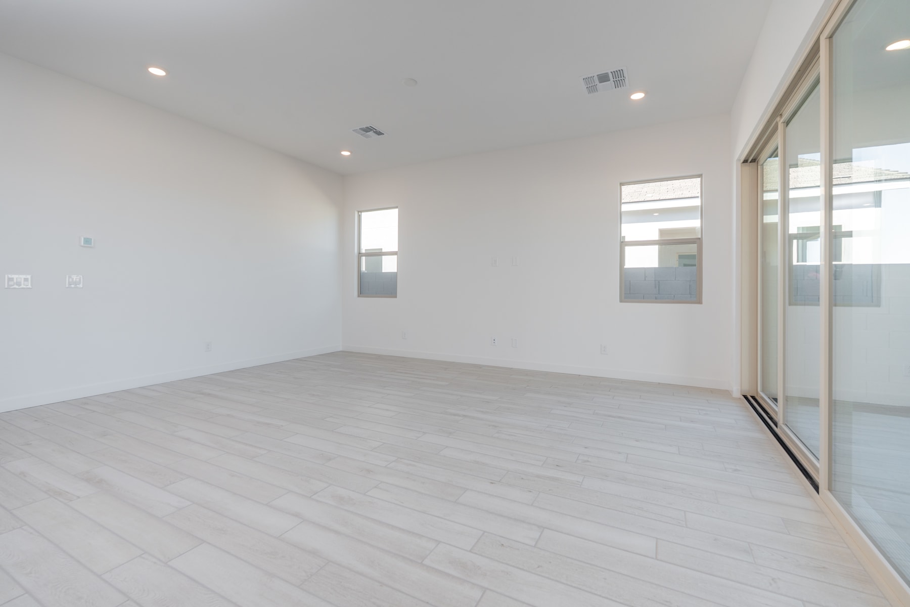 A spacious, well-lit room with white walls and a light-colored wooden floor, featuring a large window that allows natural light to flood the space.