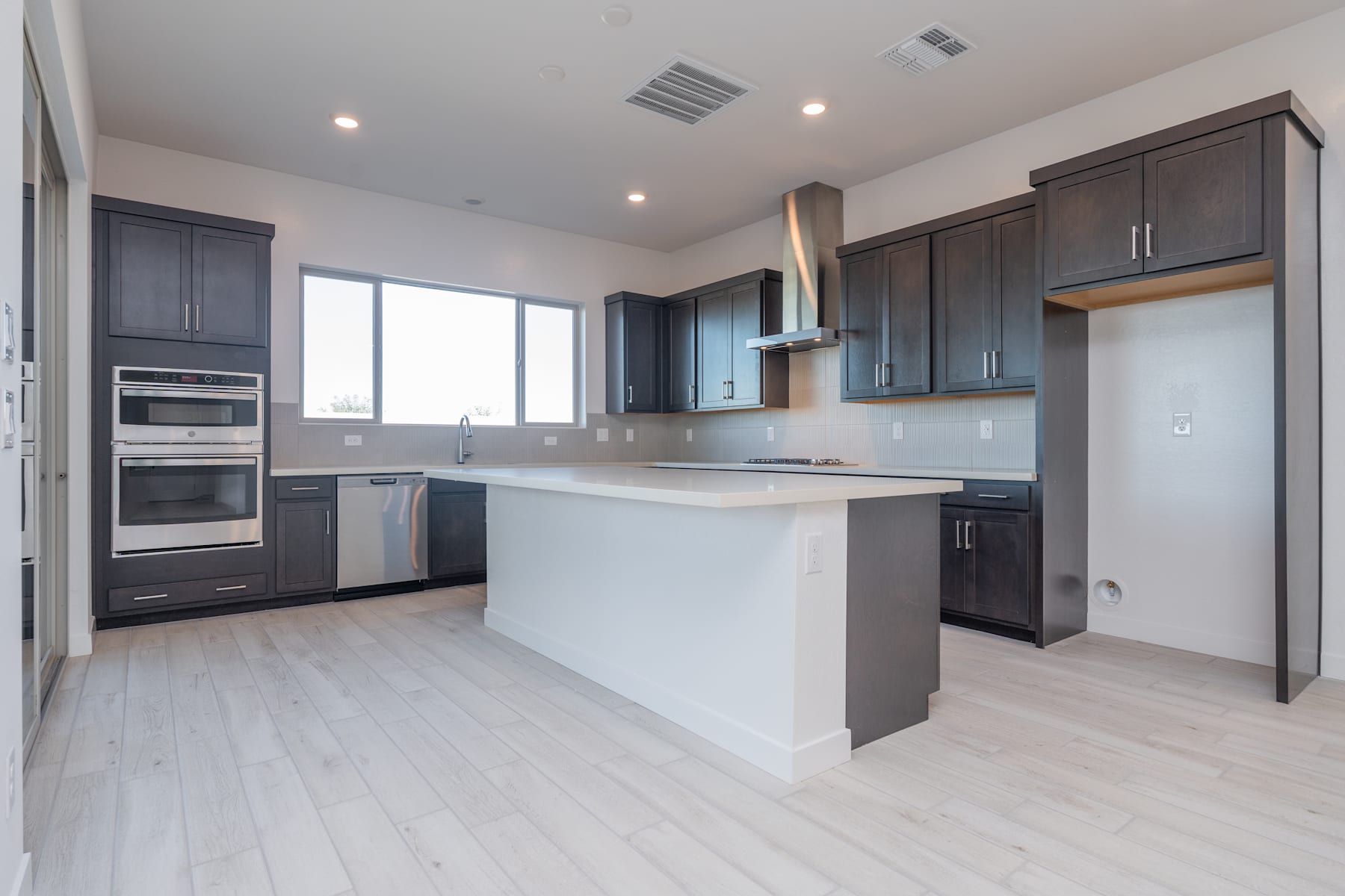 A modern, open-concept kitchen with dark cabinets, stainless steel appliances, and a white countertop island, set against a bright and airy background.