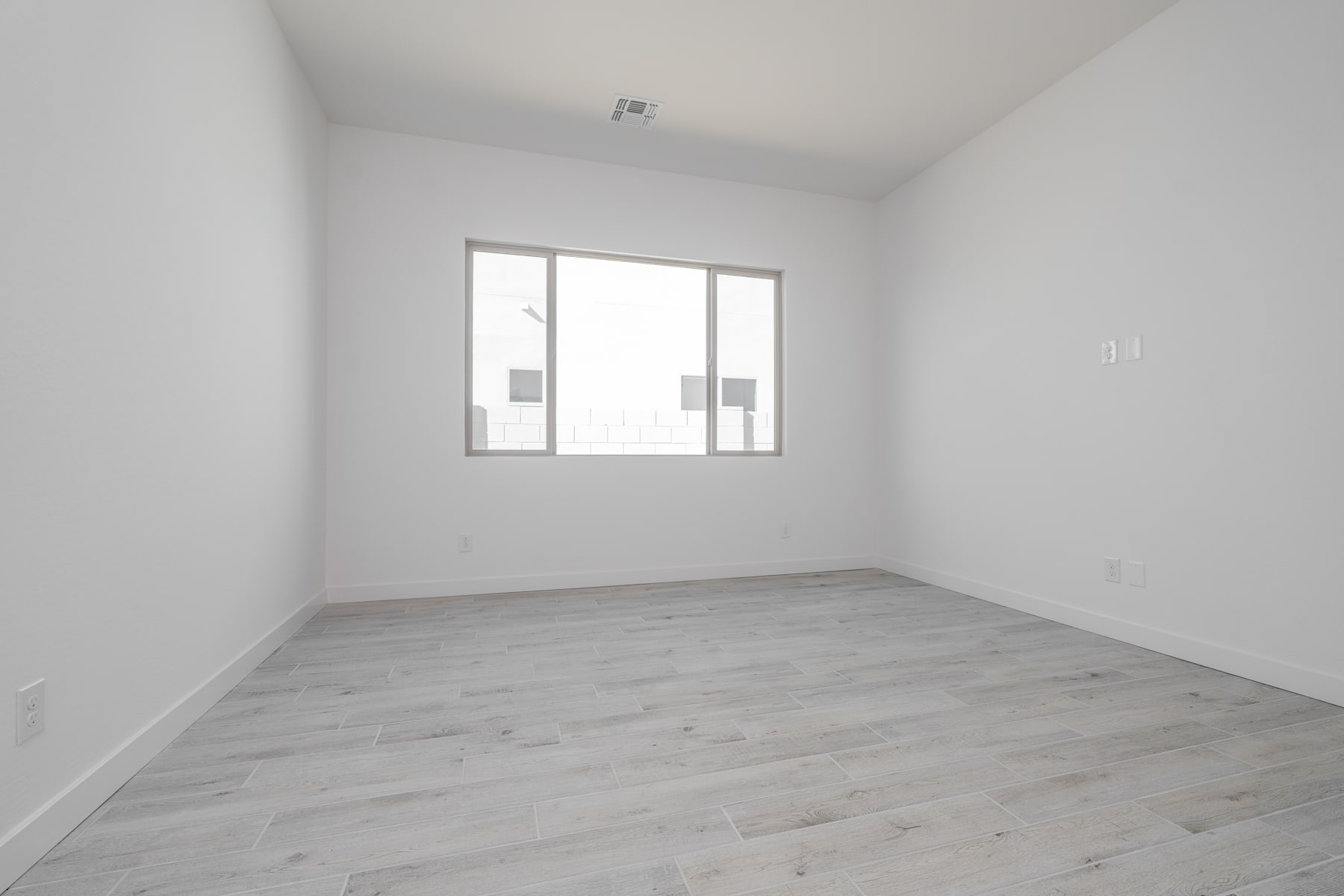 A bright, minimalist room with white walls, a large window, and a wooden floor.