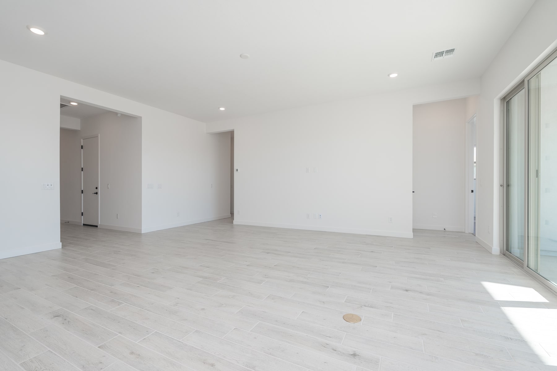 A spacious, bright room with white walls and light-colored hardwood flooring, featuring a sliding glass door leading to an outdoor area.