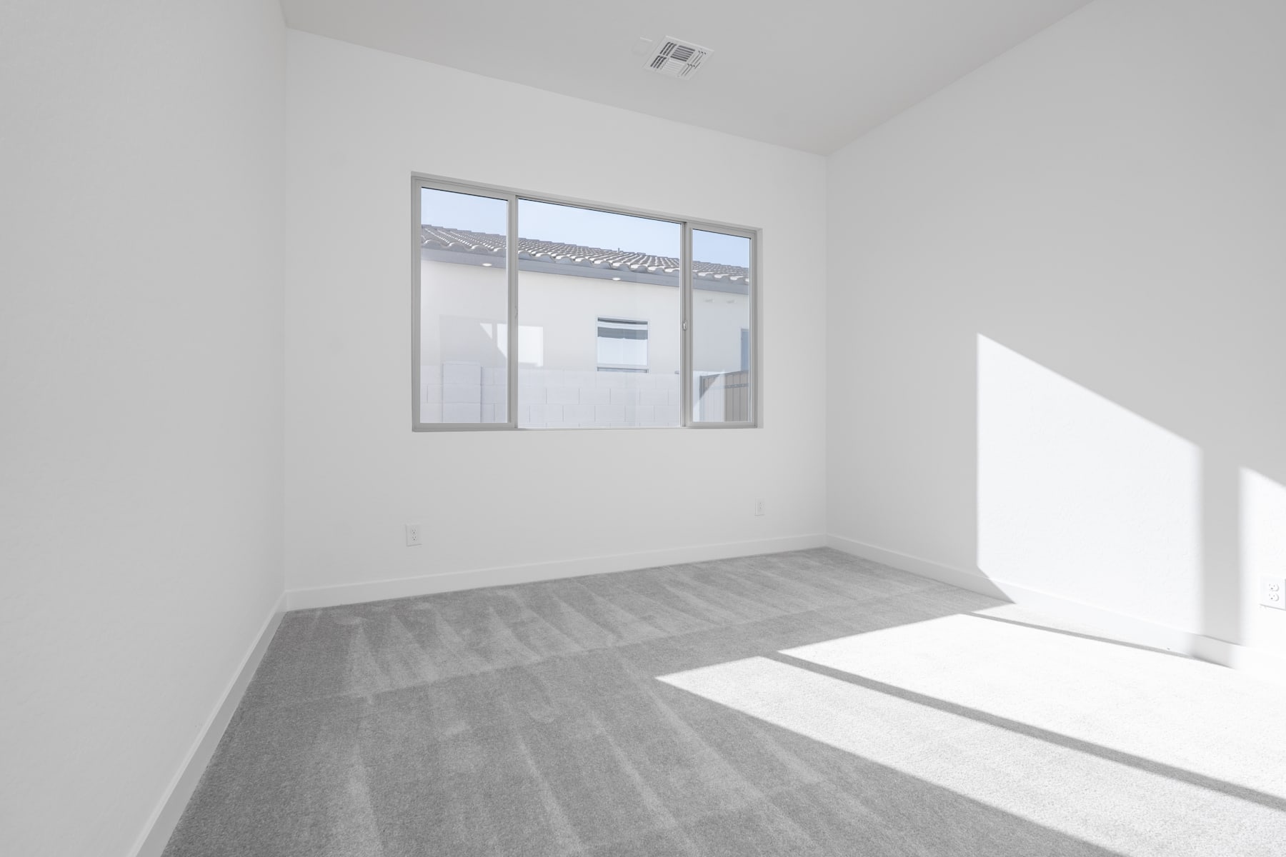 A bright, minimalist room with a large window, hardwood flooring, and a simple white wall.