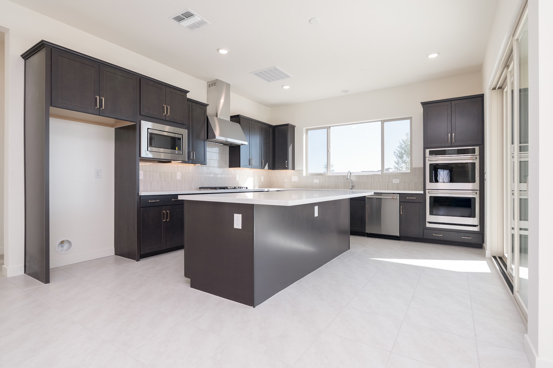 A modern, well-equipped kitchen with dark cabinets, stainless steel appliances, and a central island, set against a bright and airy background.