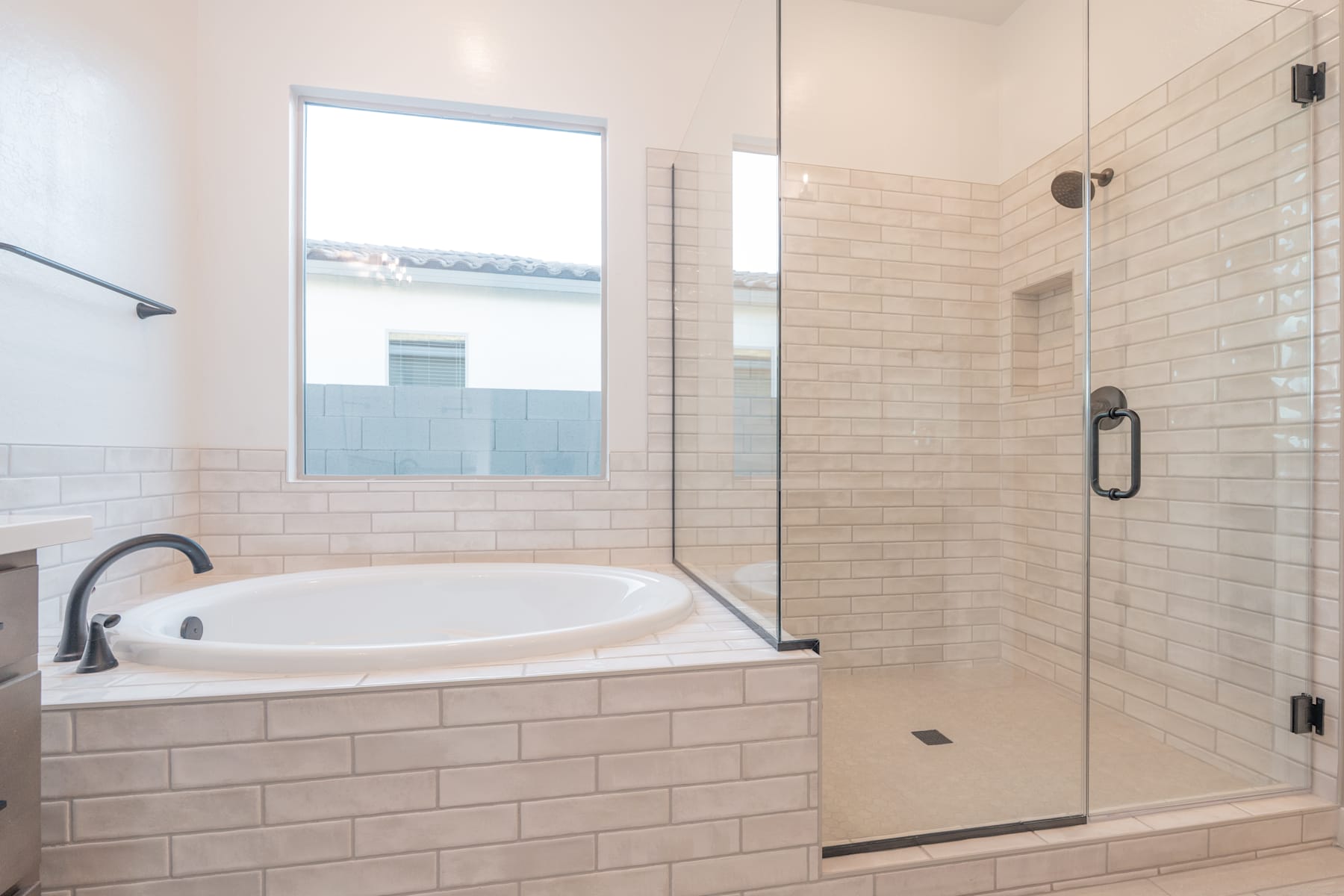 A modern bathroom with a large bathtub, a glass-enclosed shower, and a window providing natural light.