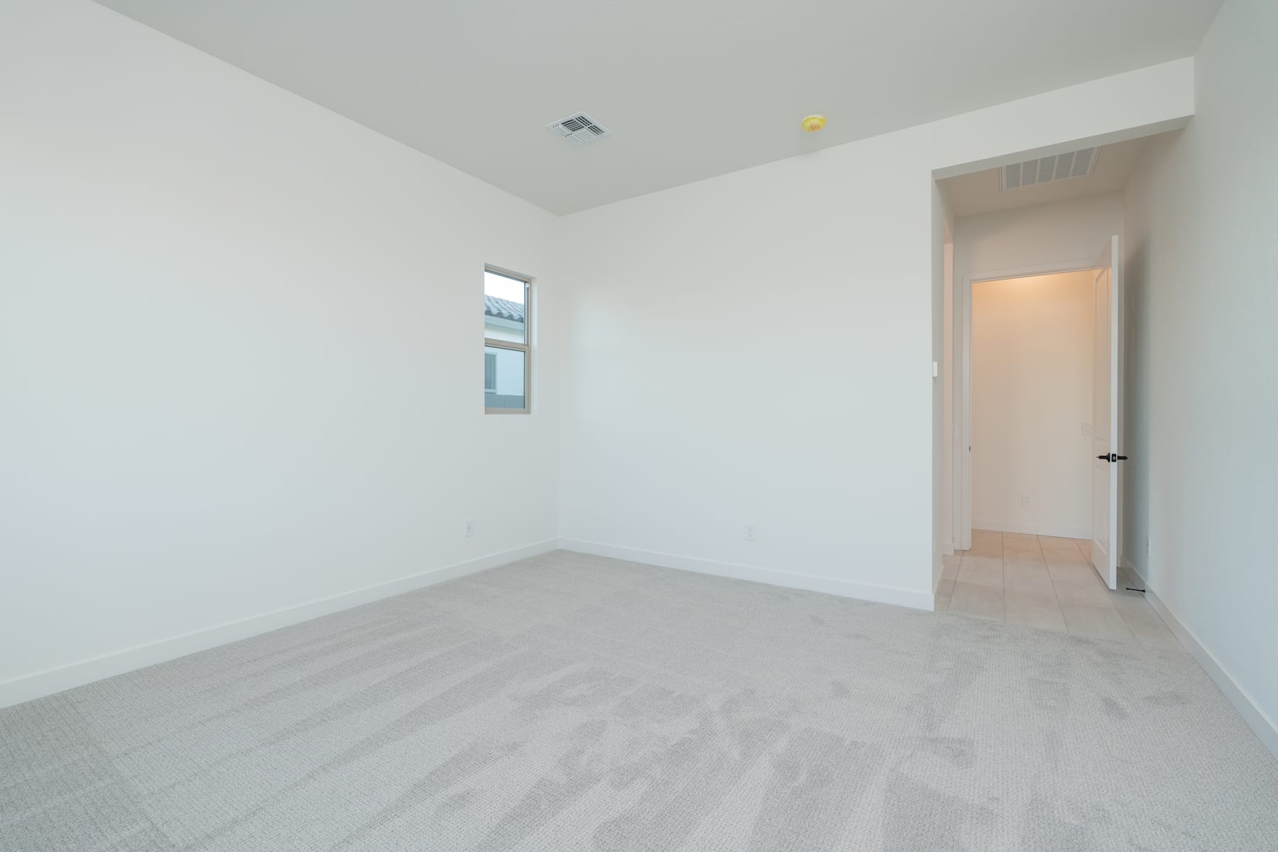 A spacious, minimalist room with white walls, a tiled floor, and a doorway leading to another room.