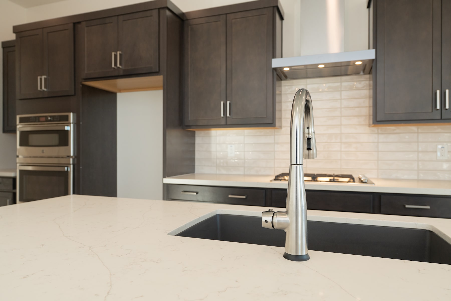 A modern kitchen with dark wood cabinets, a stainless steel sink, and a white countertop.