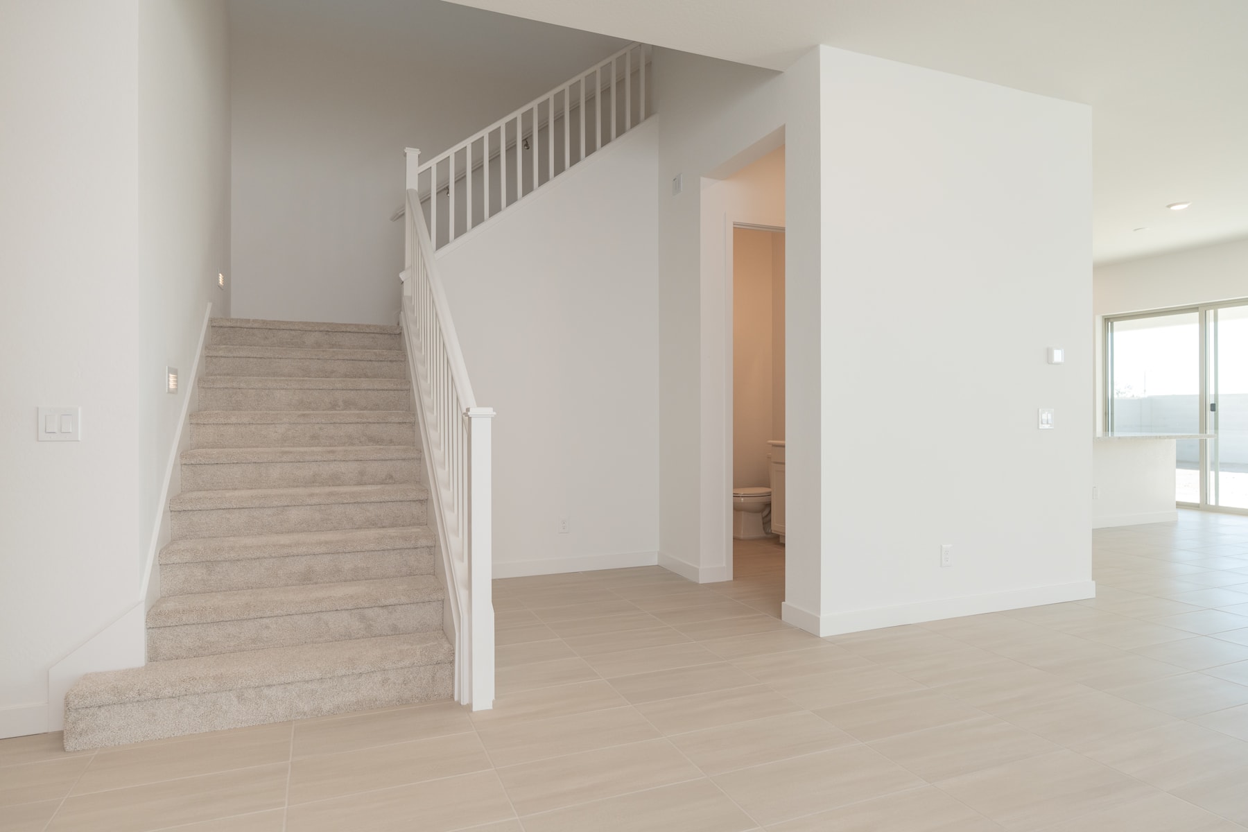 A bright and spacious interior with a staircase leading up to a doorway, surrounded by clean white walls and light-colored hardwood floors.
