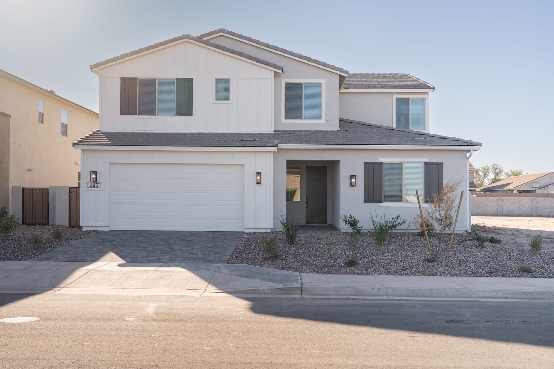 A two-story residential house with a garage, surrounded by a paved driveway and landscaped yard, set against a clear blue sky.
