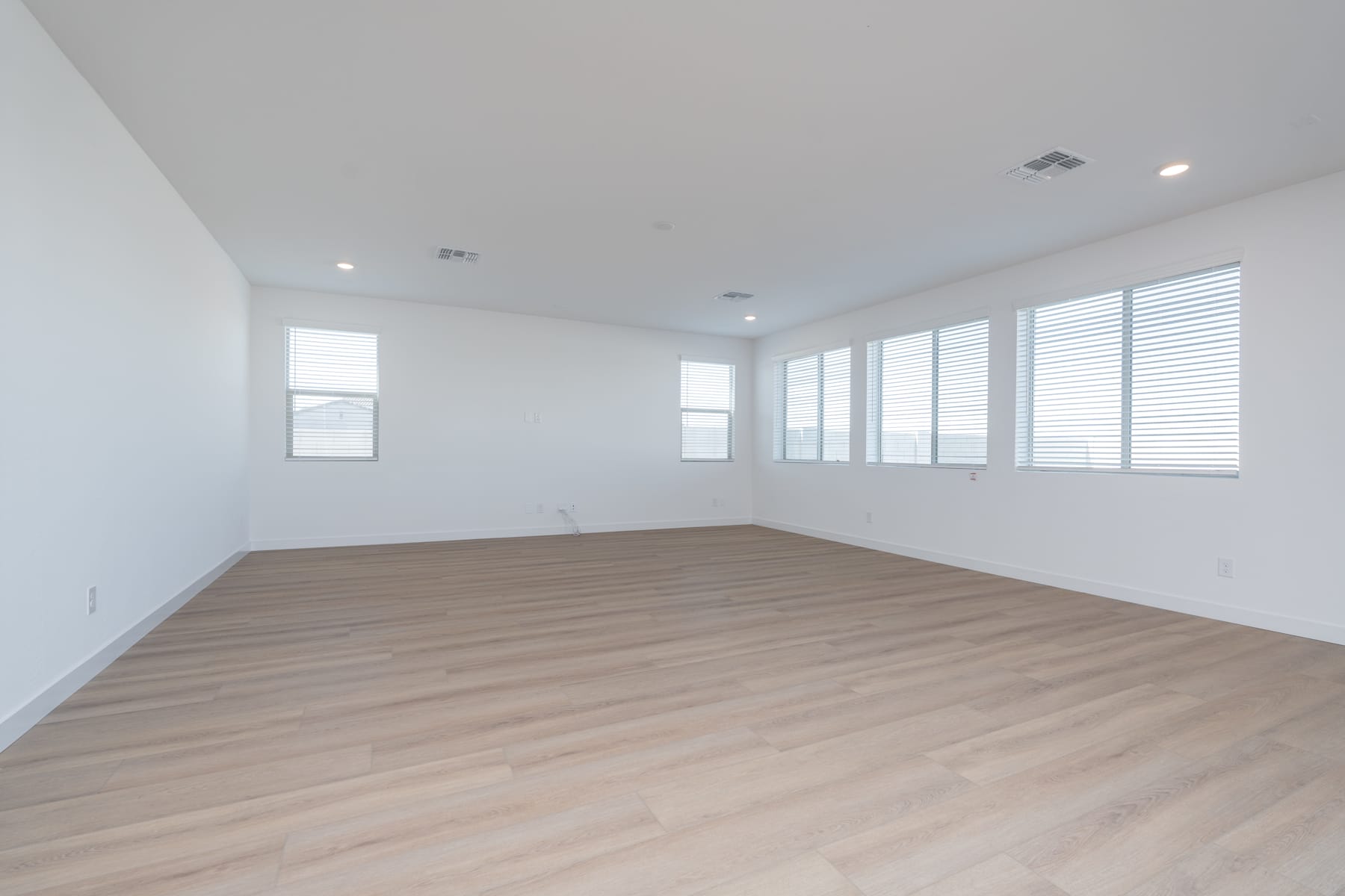A spacious, well-lit room with white walls, large windows, and a wooden floor.