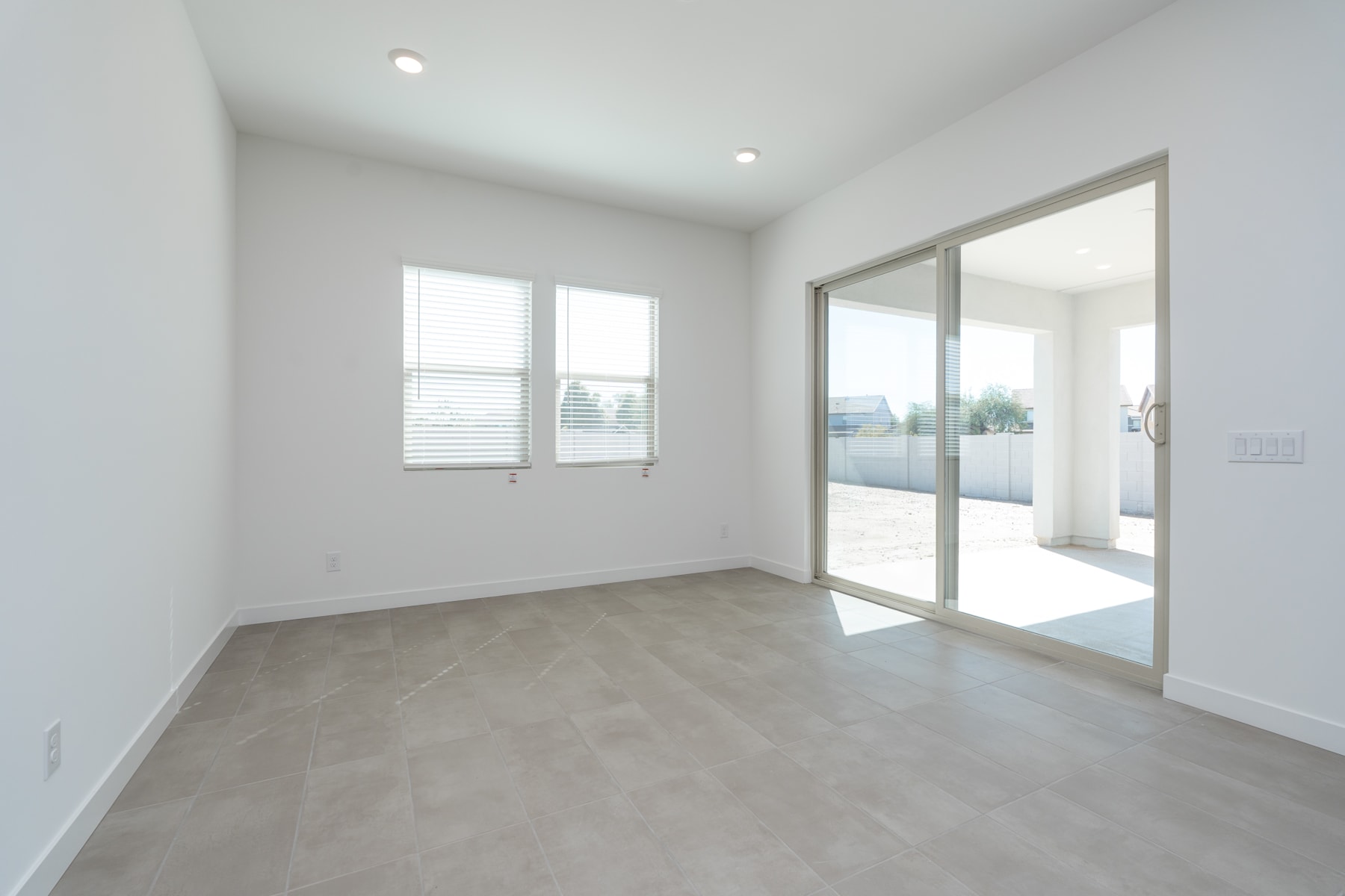 A bright, minimalist room with large windows, a sliding glass door, and a smooth concrete floor.