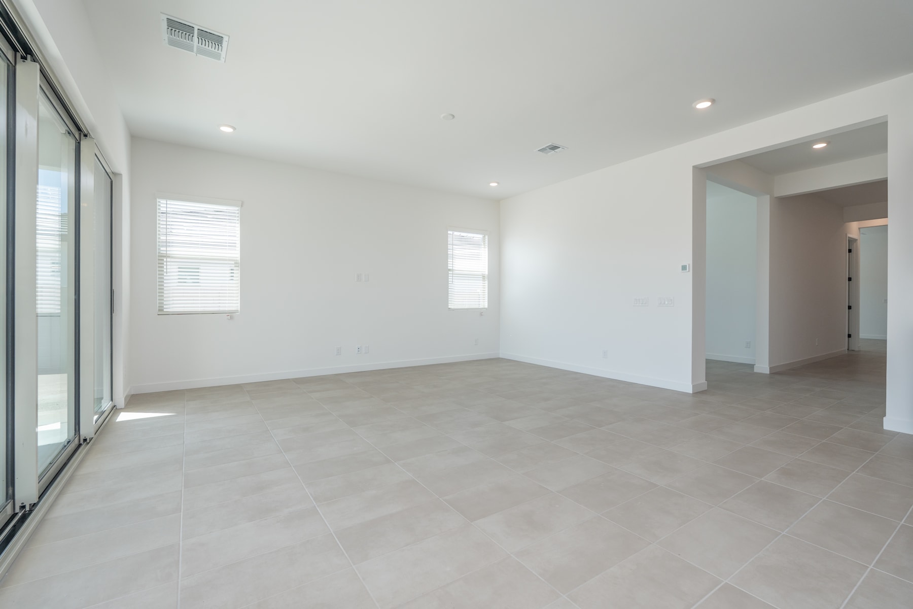 A spacious, minimalist room with large windows, light-colored tile flooring, and recessed lighting in the ceiling.