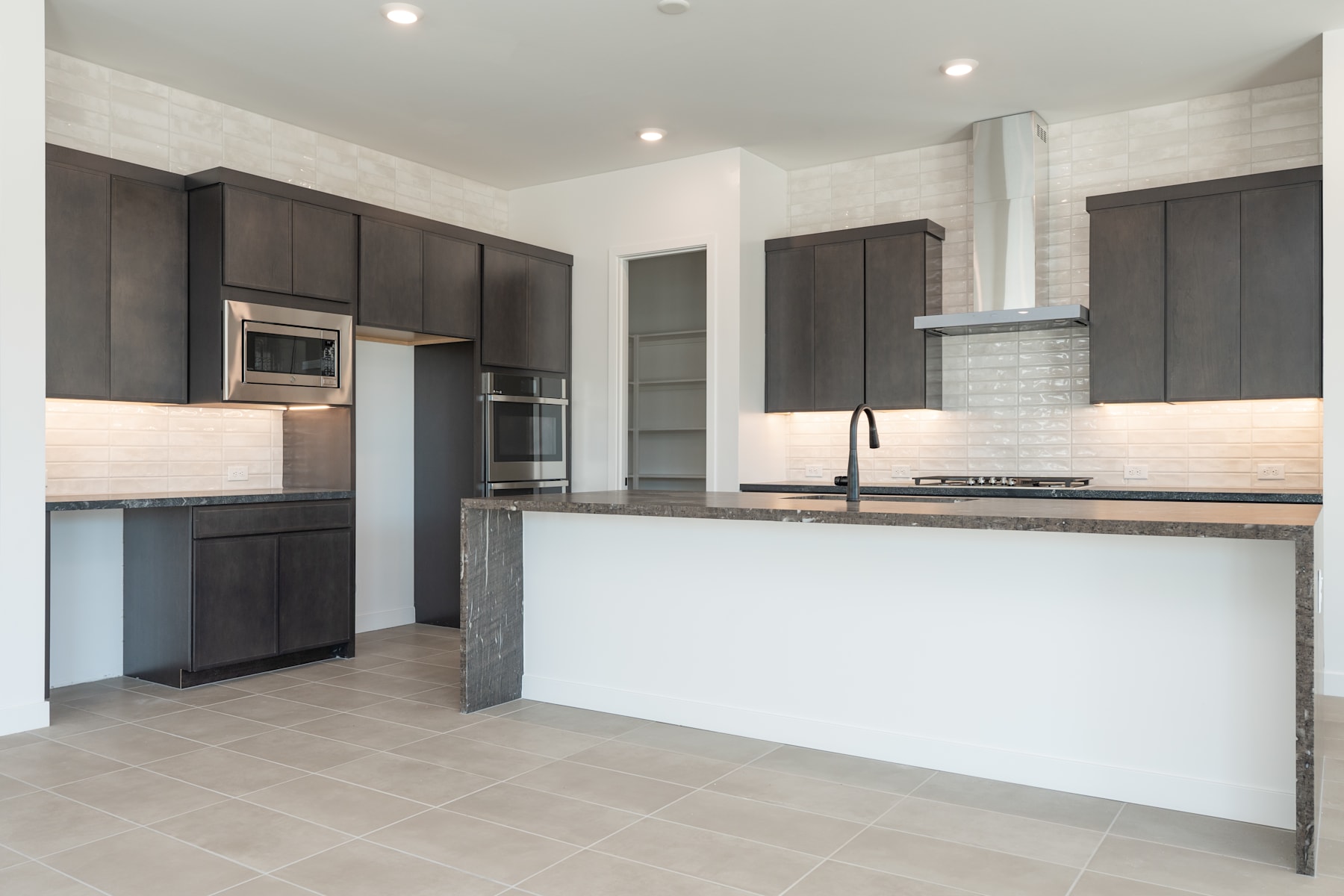 A modern, open-concept kitchen with dark cabinets, a white countertop, and a tiled floor.