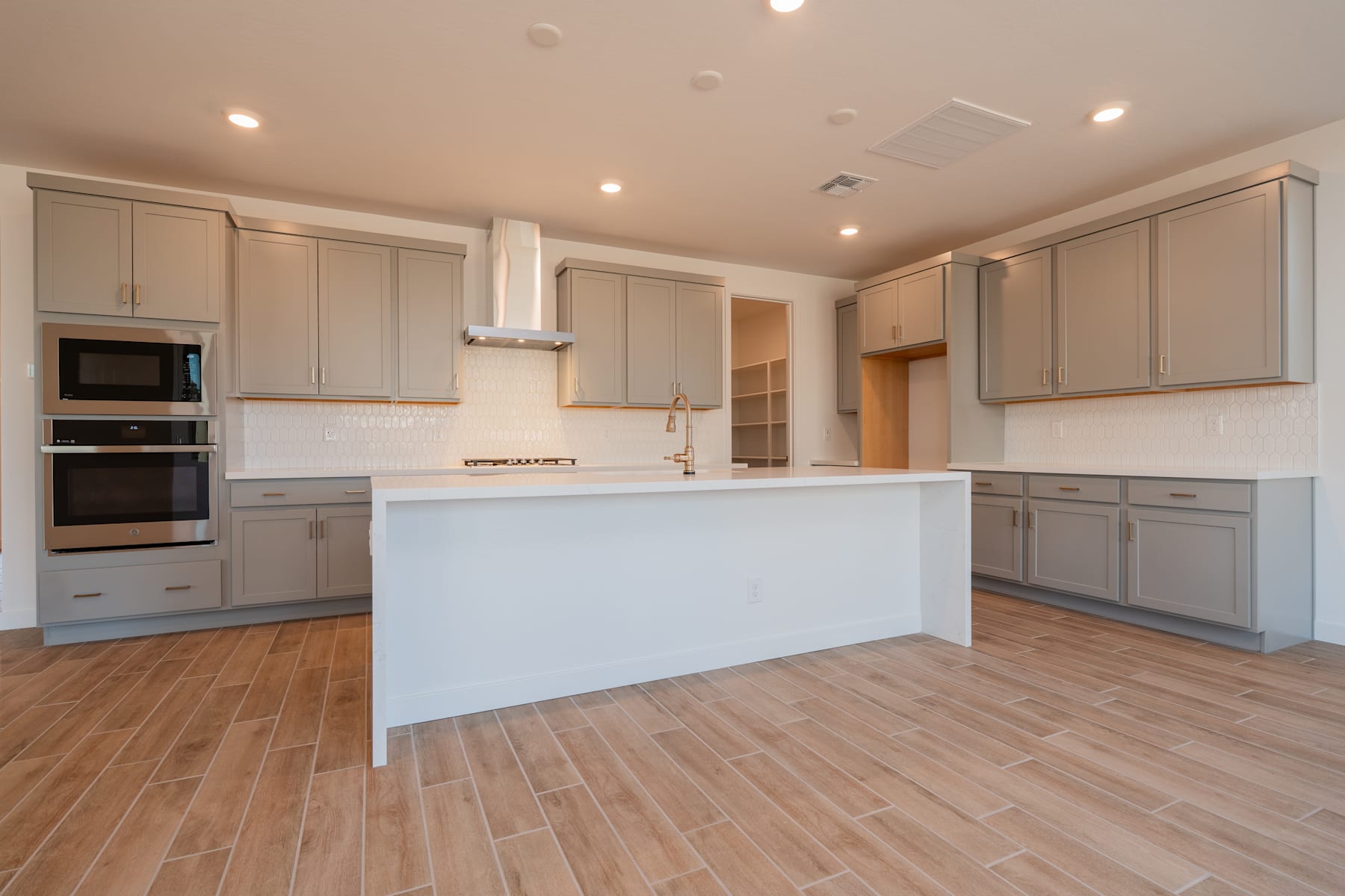 A modern, open-concept kitchen with light-colored cabinets, a white island, and hardwood flooring.