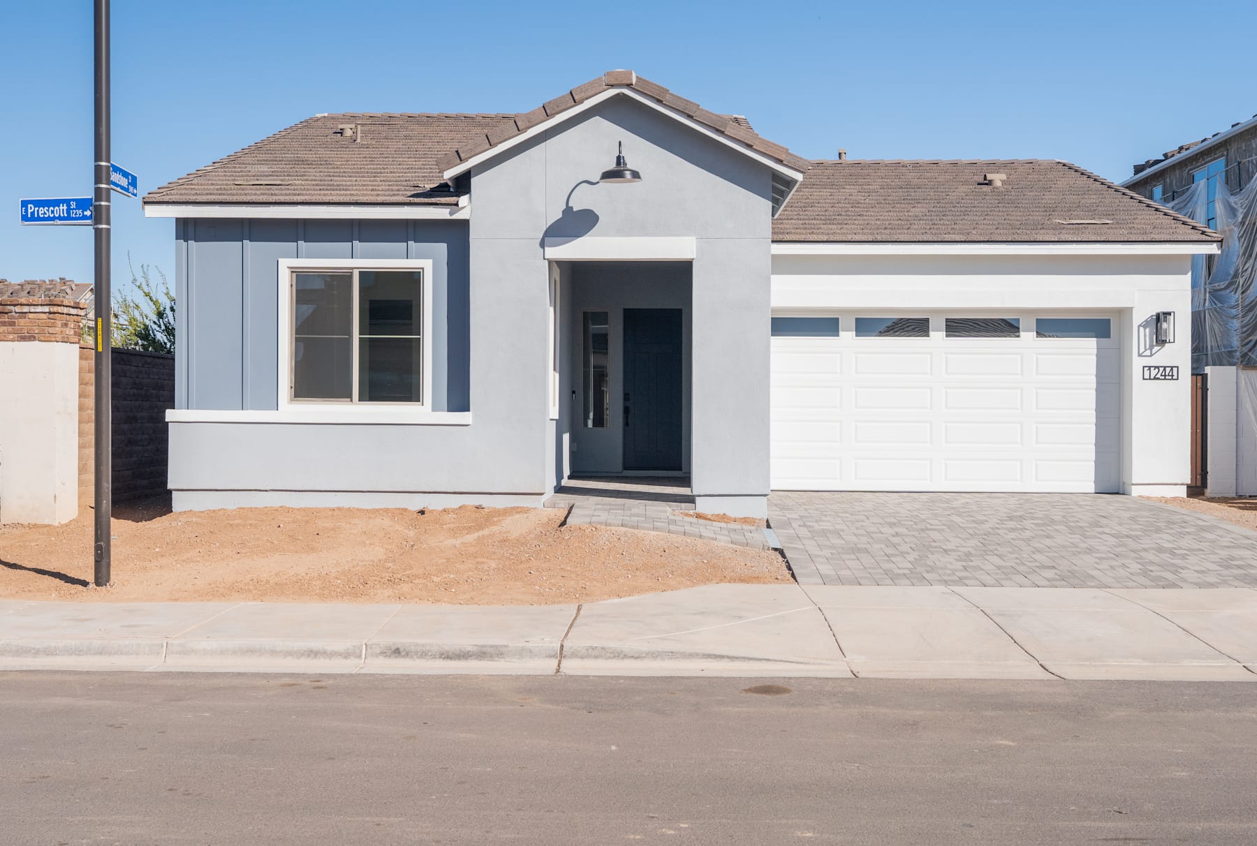 A newly constructed single-story house with a garage, situated on a paved street with a clear blue sky in the background.