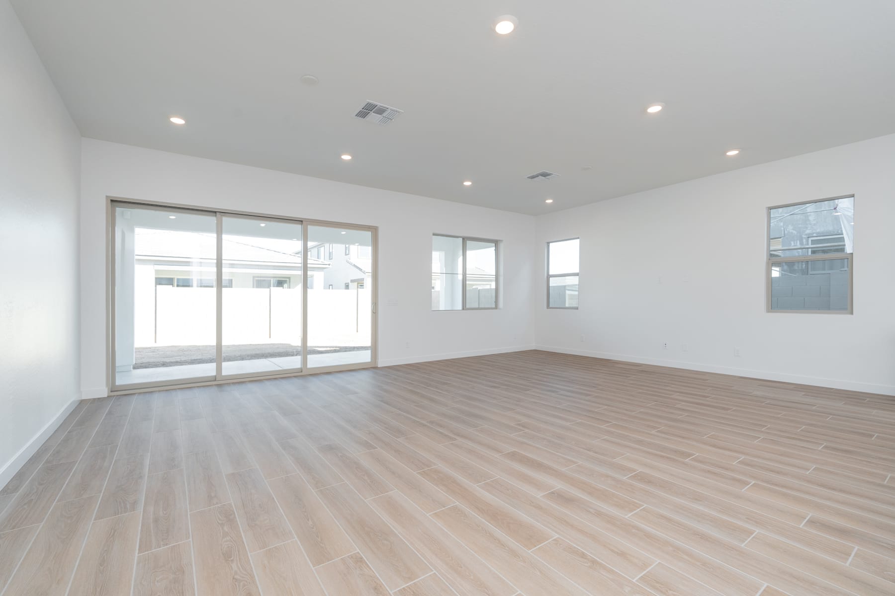 A spacious, well-lit room with large windows, a hardwood floor, and recessed lighting fixtures in the ceiling.