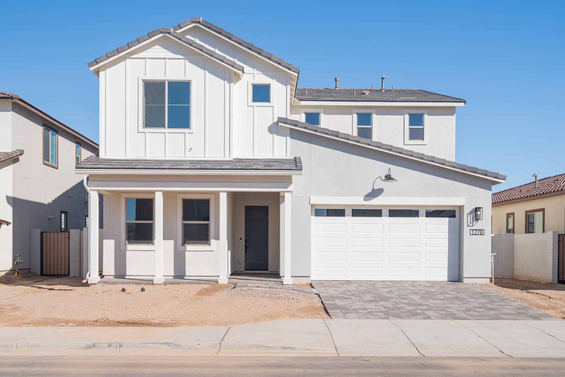 A modern, two-story white house with a garage door, surrounded by a paved driveway and a clear blue sky in the background.