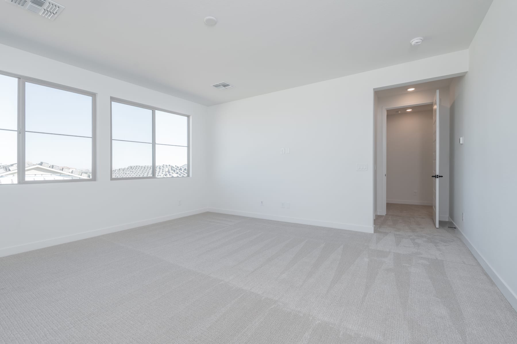 A spacious, bright room with large windows, a hardwood floor, and a doorway leading to another area.
