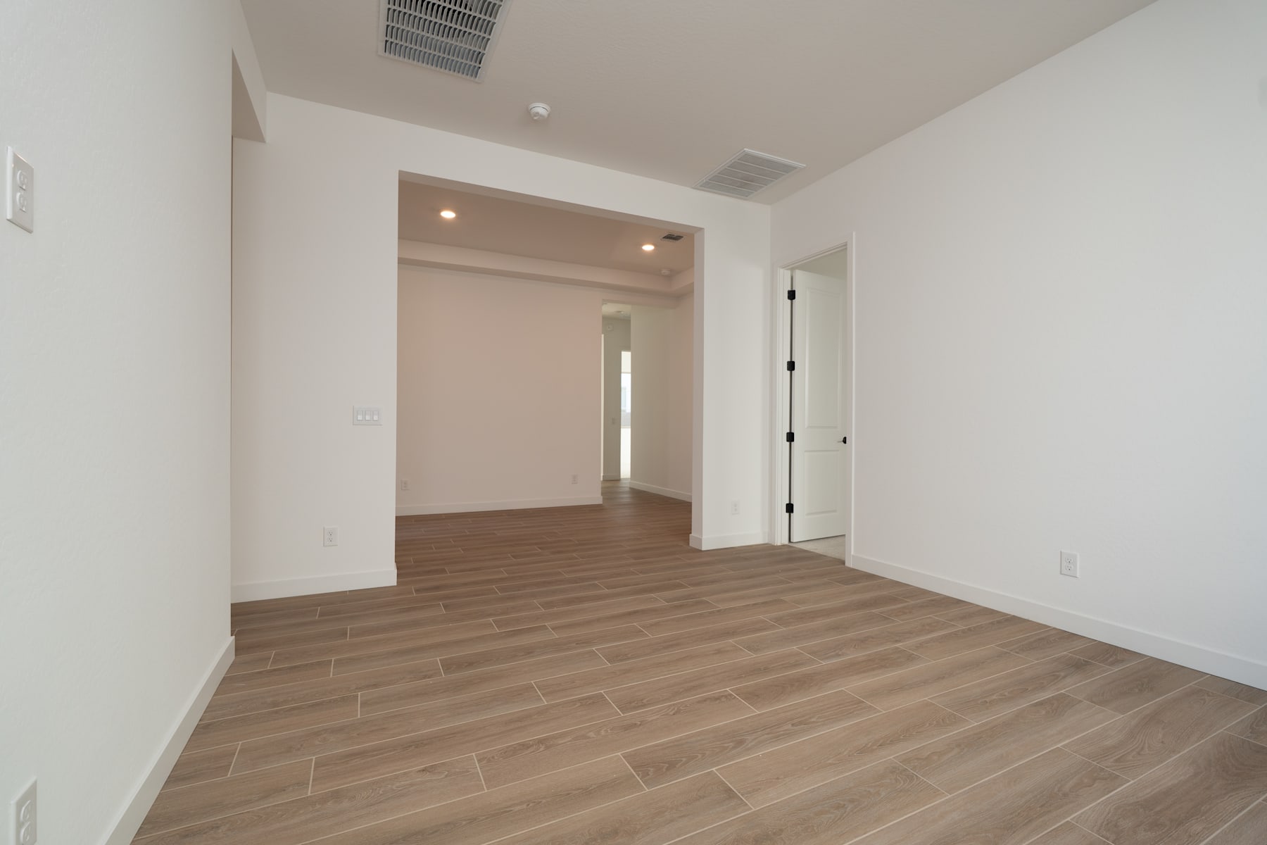 A spacious, well-lit room with a wooden floor and a doorway leading to another area.