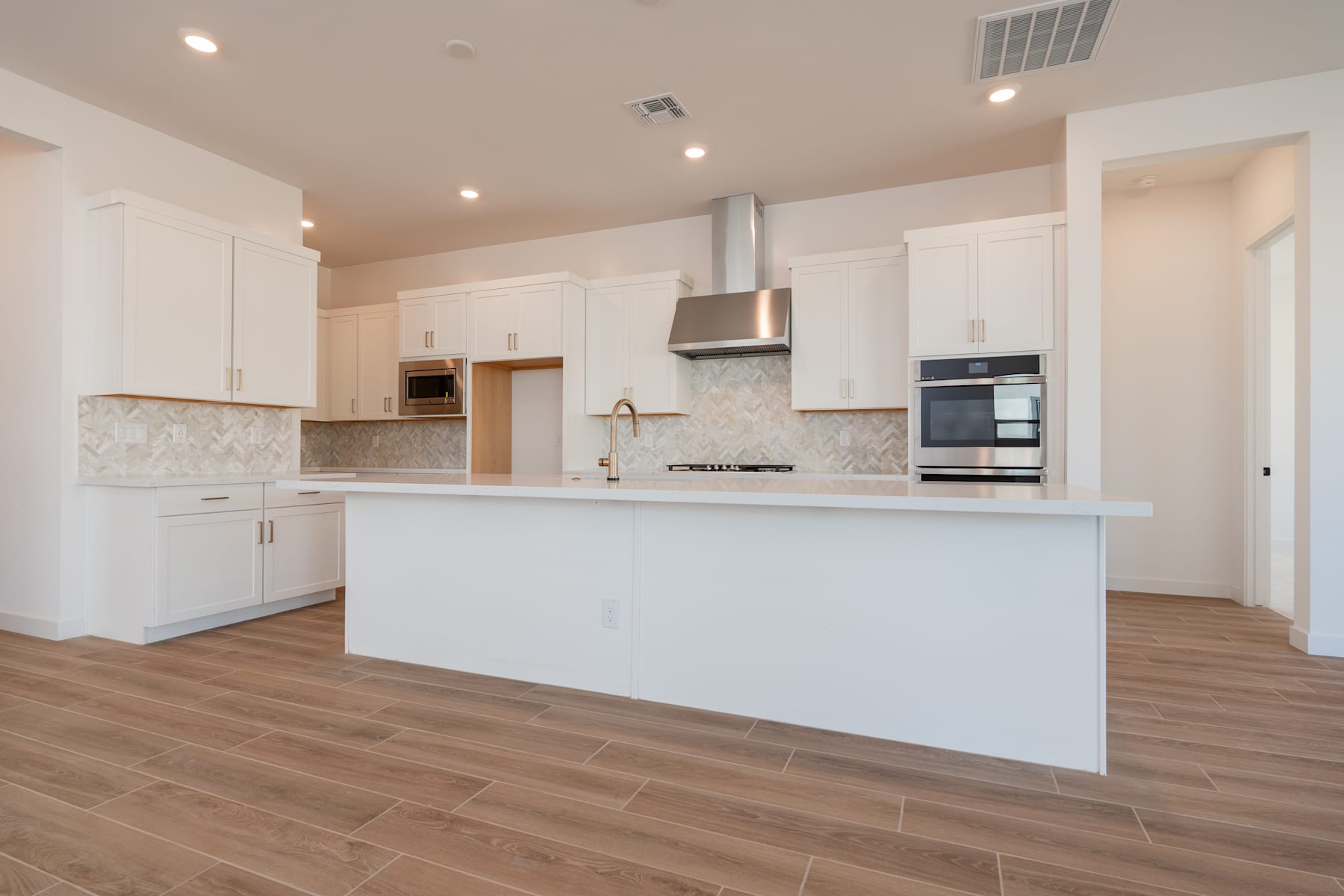 A modern, open-concept kitchen with white cabinets, stainless steel appliances, and a large central island with a wooden floor.