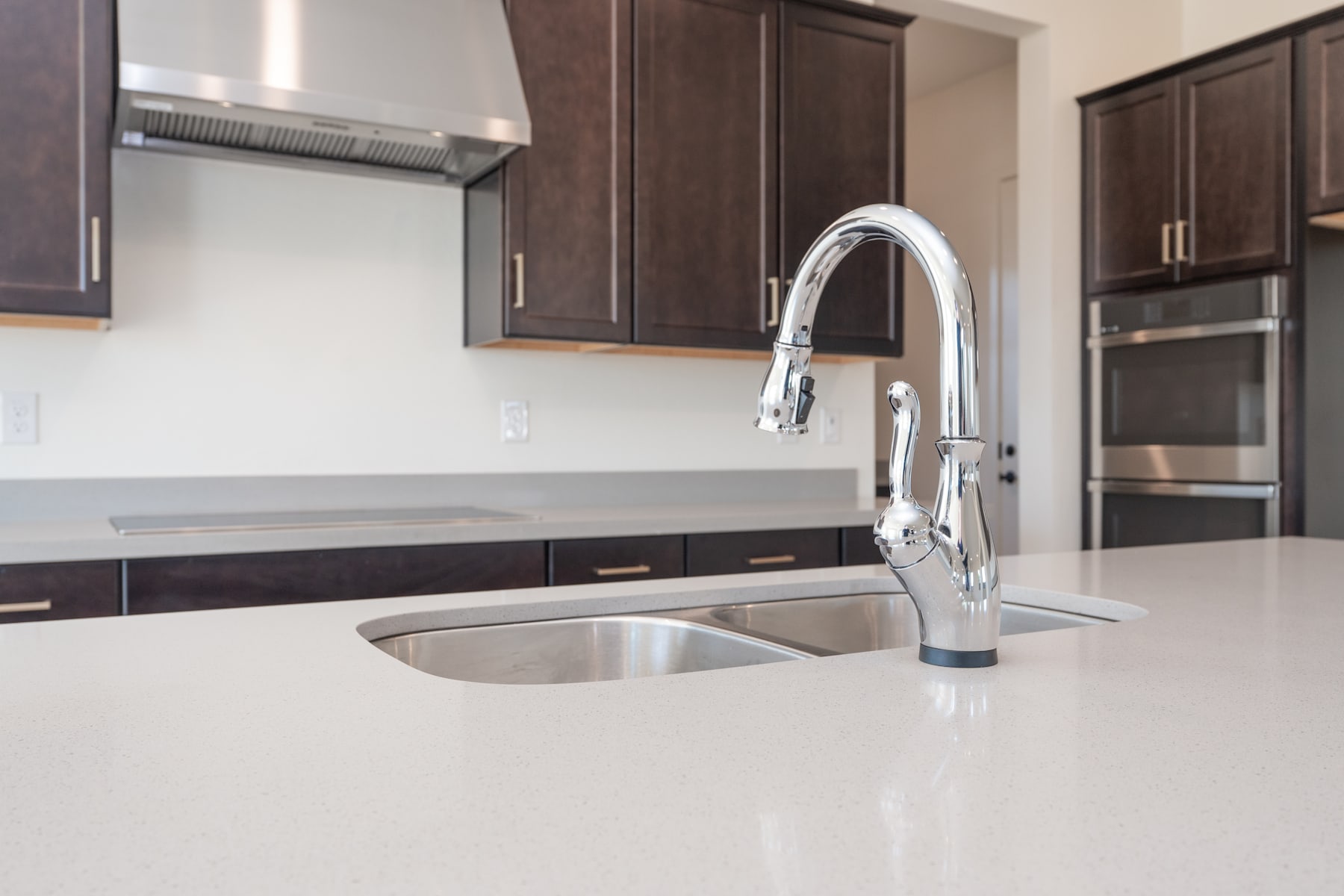 A modern kitchen with dark wood cabinets, a stainless steel sink, and a chrome faucet set against a white countertop.