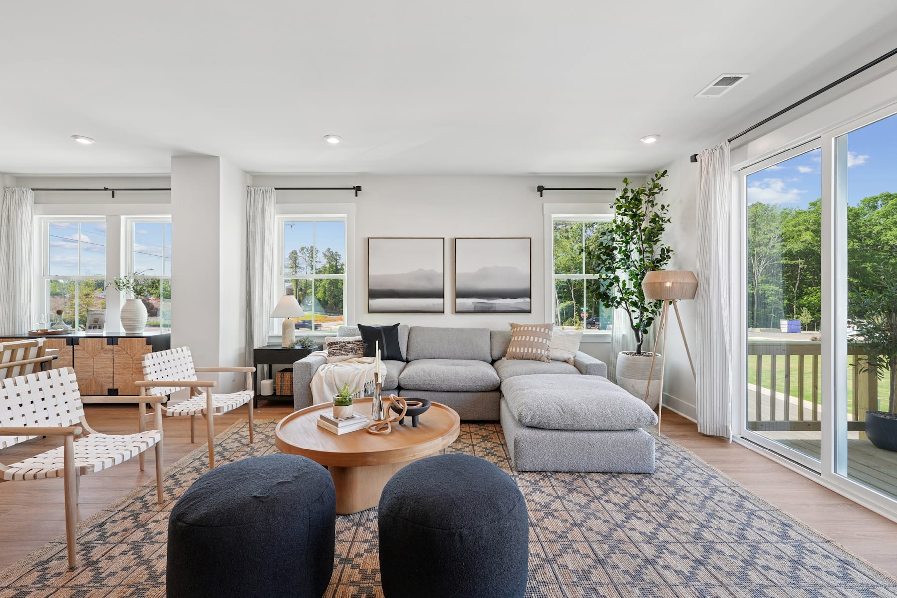 A spacious and modern living room with large windows overlooking a lush outdoor area, featuring a comfortable gray sectional sofa, a wooden coffee table, and decorative accents that create a warm and inviting atmosphere.