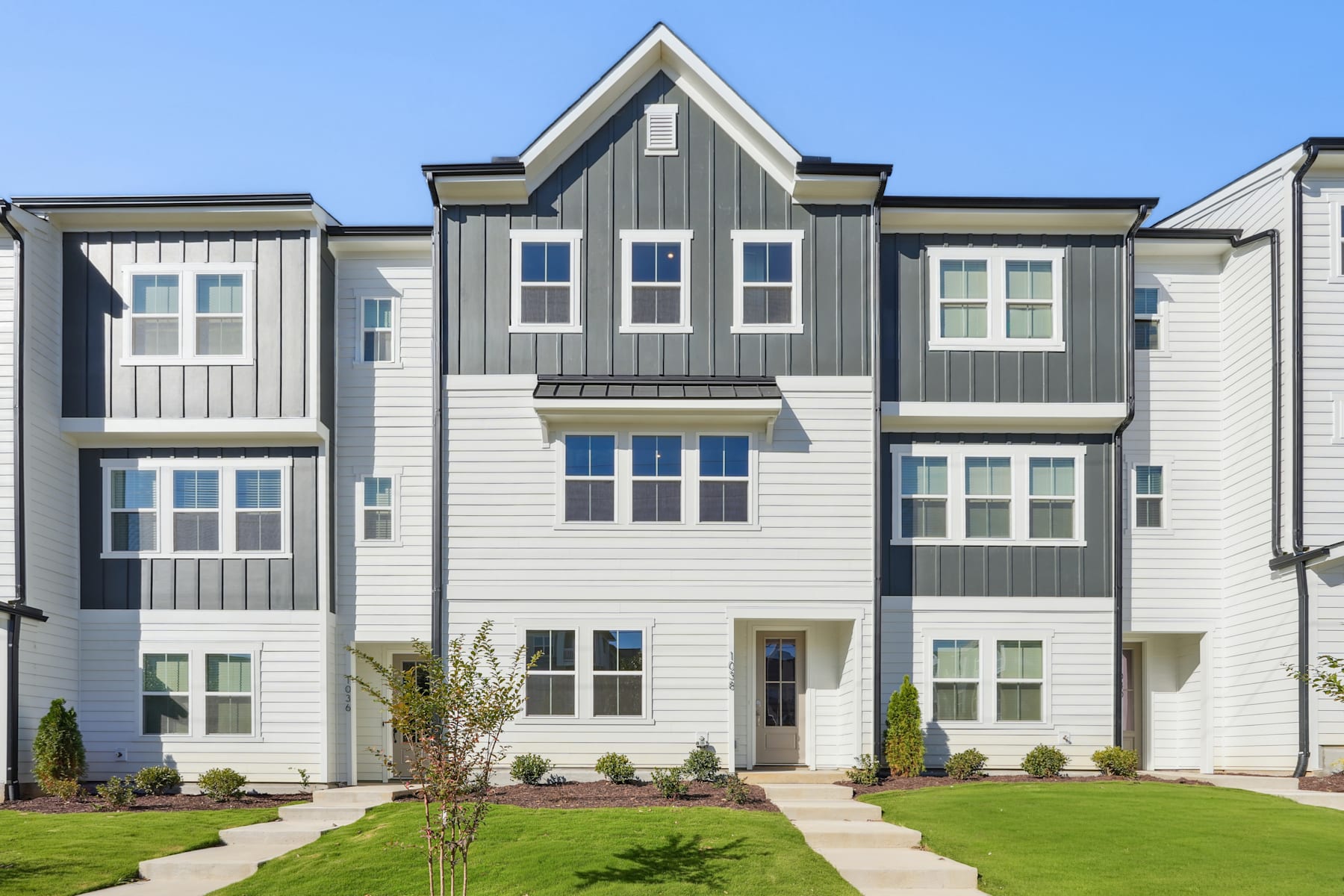 A multi-story residential building with a gray and white exterior, surrounded by a well-manicured lawn and landscaping.