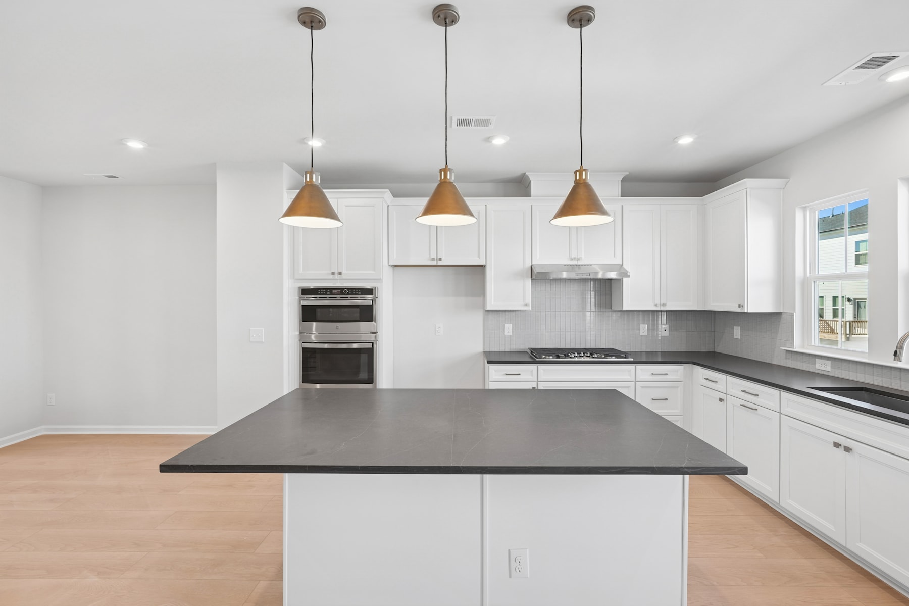 A modern, minimalist kitchen with white cabinets, a dark countertop, and pendant lights hanging above the central island.