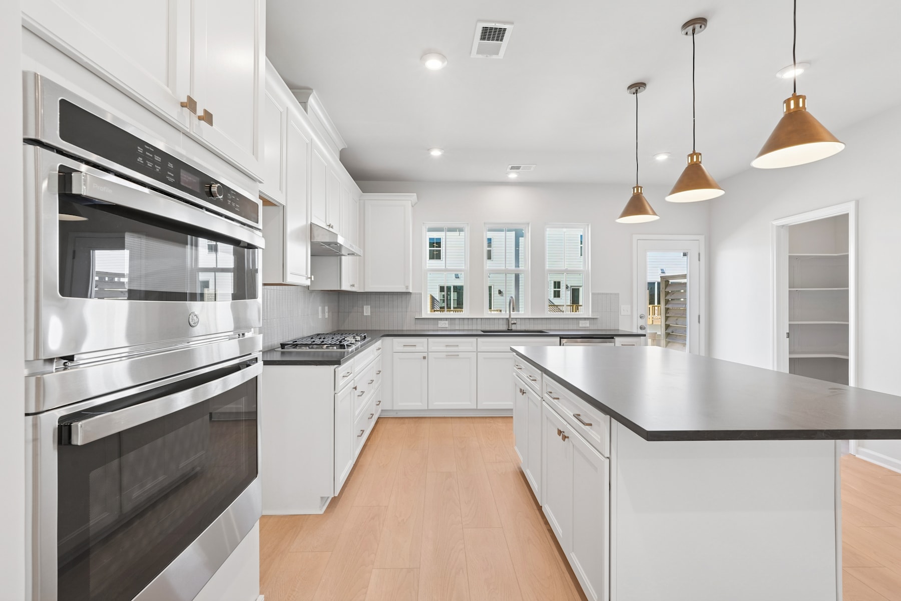 A modern, well-lit kitchen with white cabinets, stainless steel appliances, and pendant lighting fixtures, set against a hardwood floor.