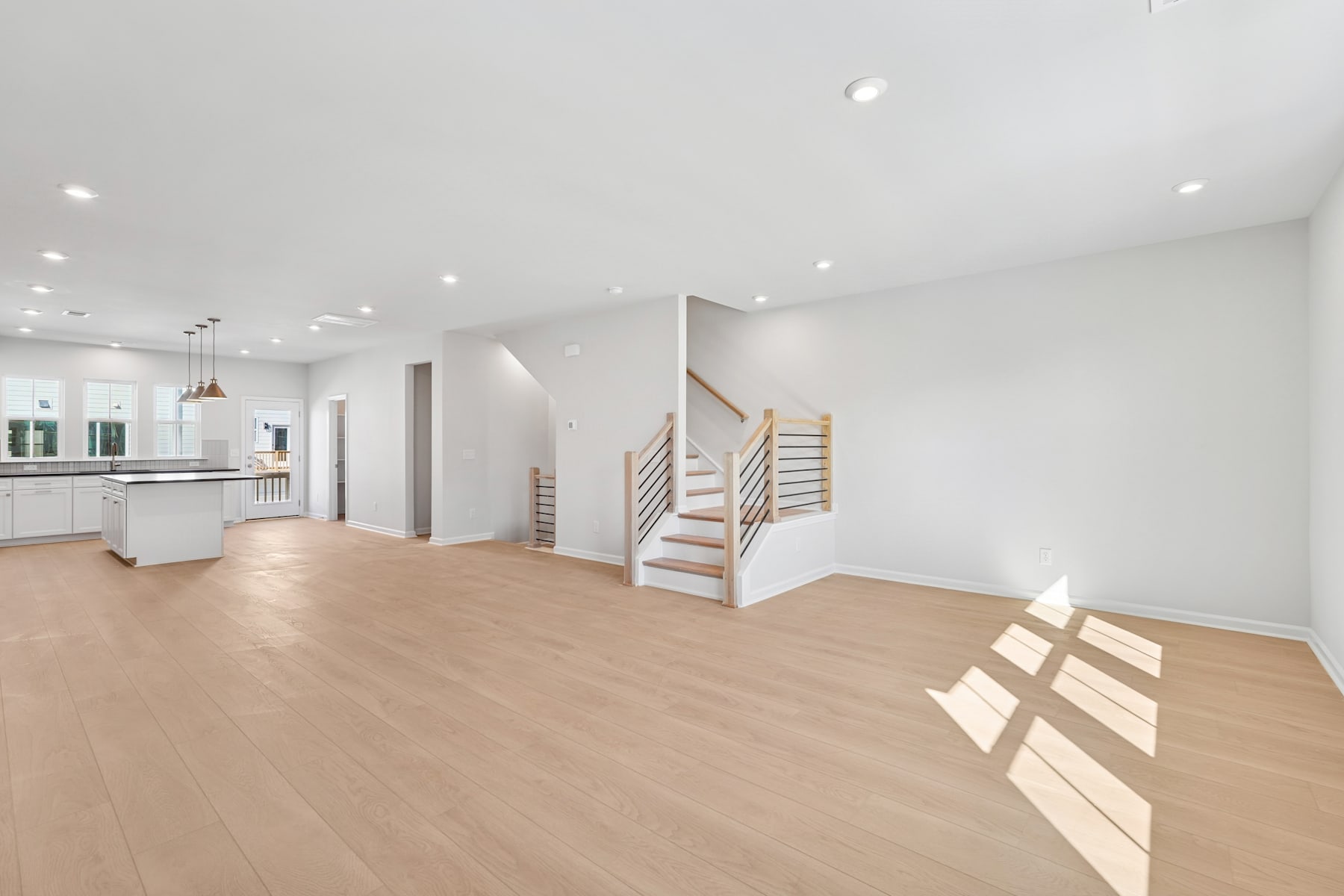 A spacious, open-concept living area with a modern kitchen, wooden floors, and a staircase leading to an upper level.
