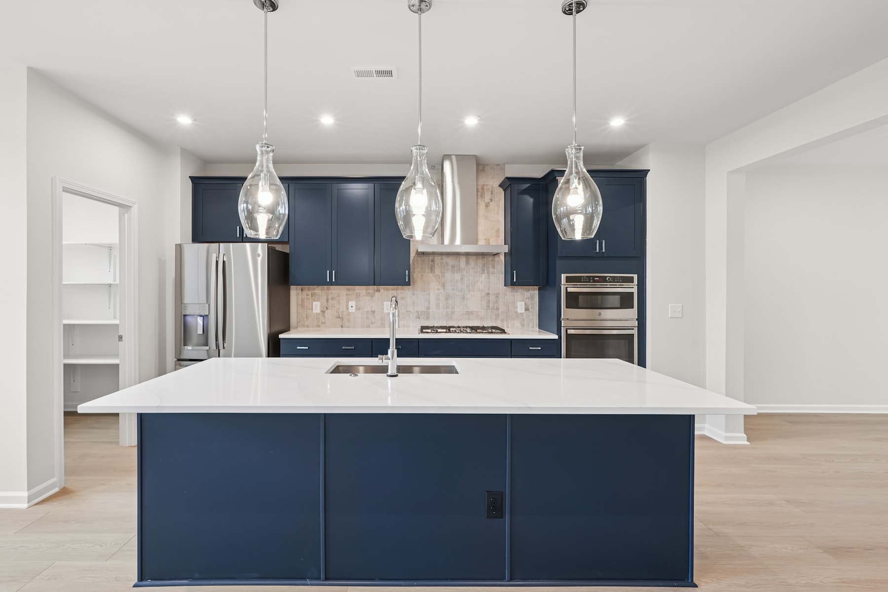 A modern, open-concept kitchen with a large white island, navy blue cabinets, and pendant lighting fixtures that create a sleek and stylish atmosphere.