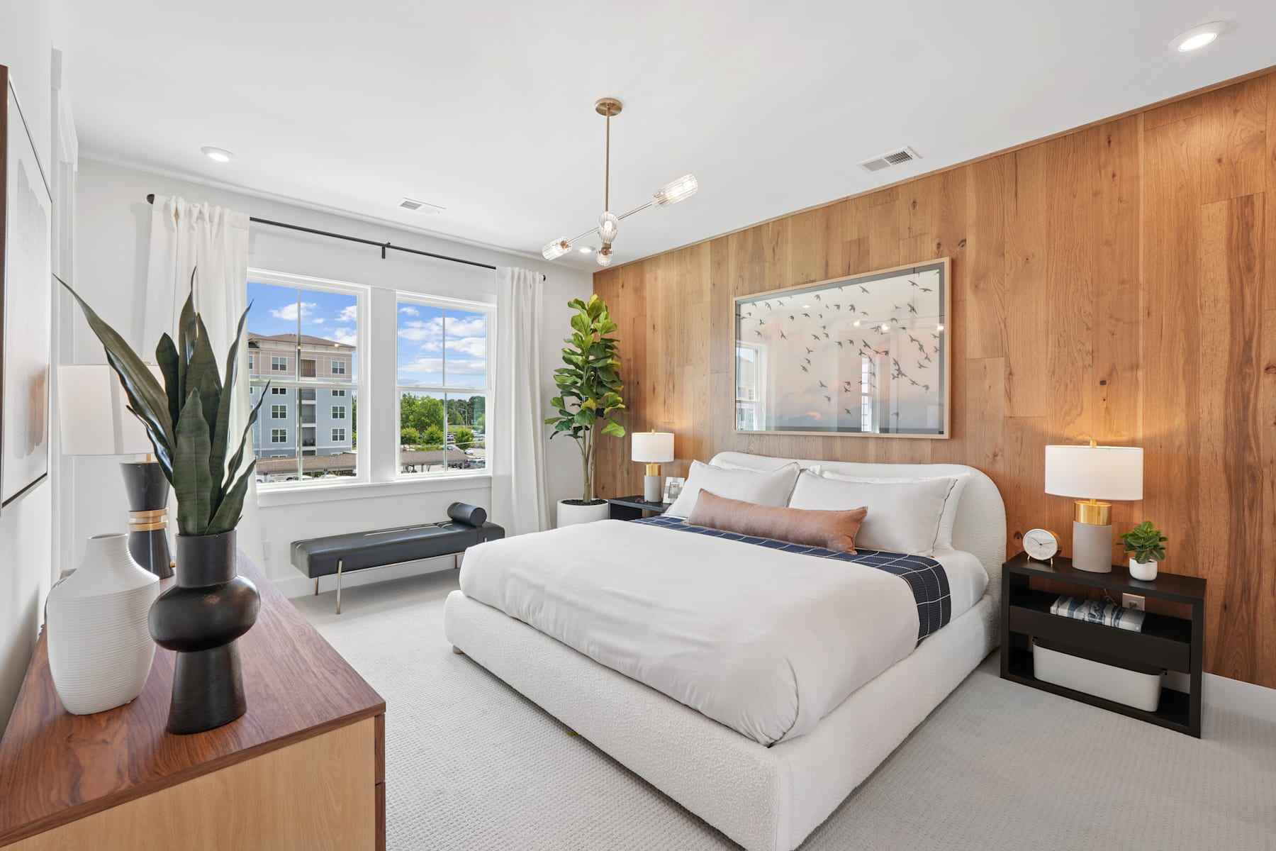 A cozy and modern bedroom with wooden paneled walls, a large bed, and a window overlooking a scenic outdoor view.