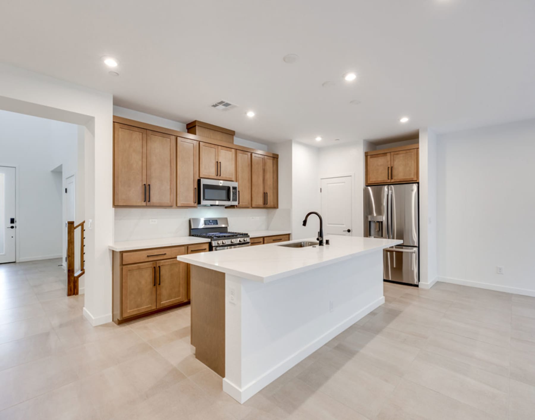 A modern, open-concept kitchen with light wood cabinets, a white island, and stainless steel appliances, set against a bright and airy background.