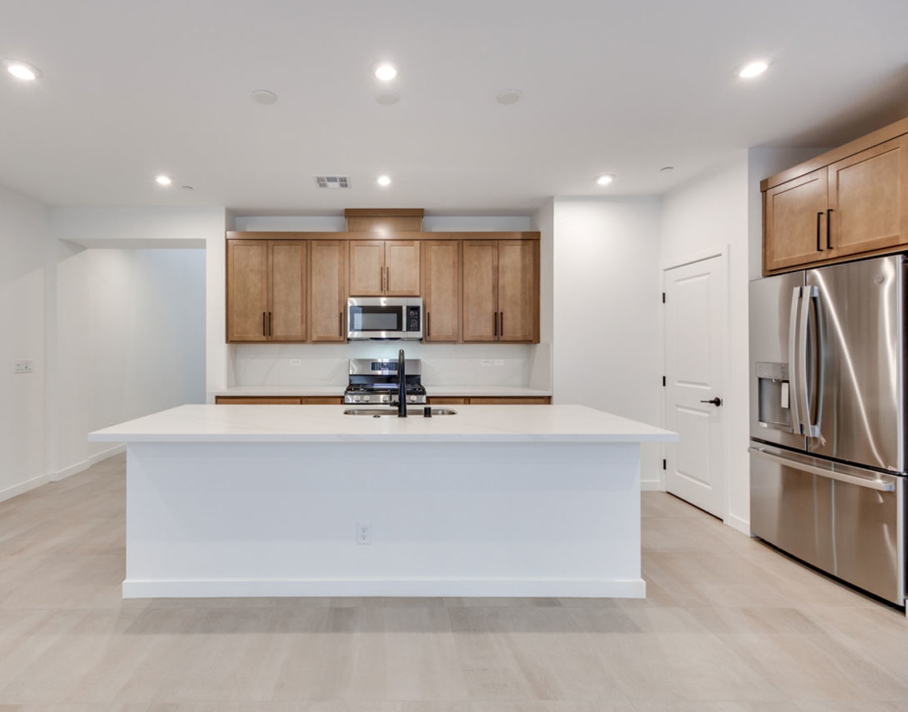 A modern, open-concept kitchen with white countertops, wooden cabinets, and stainless steel appliances, set against a bright and airy background.