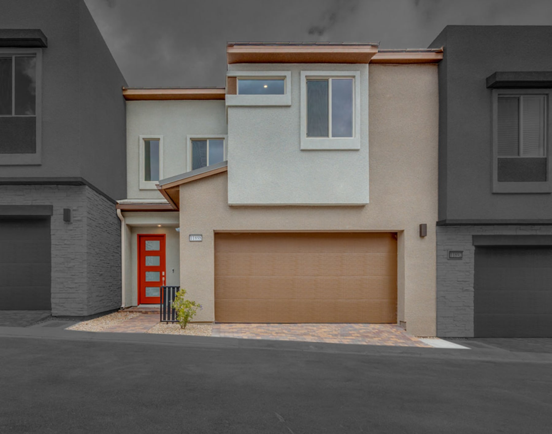 A modern, two-story residential building with a garage door, a red front door, and a minimalist architectural design featuring a mix of neutral colors and wood accents.