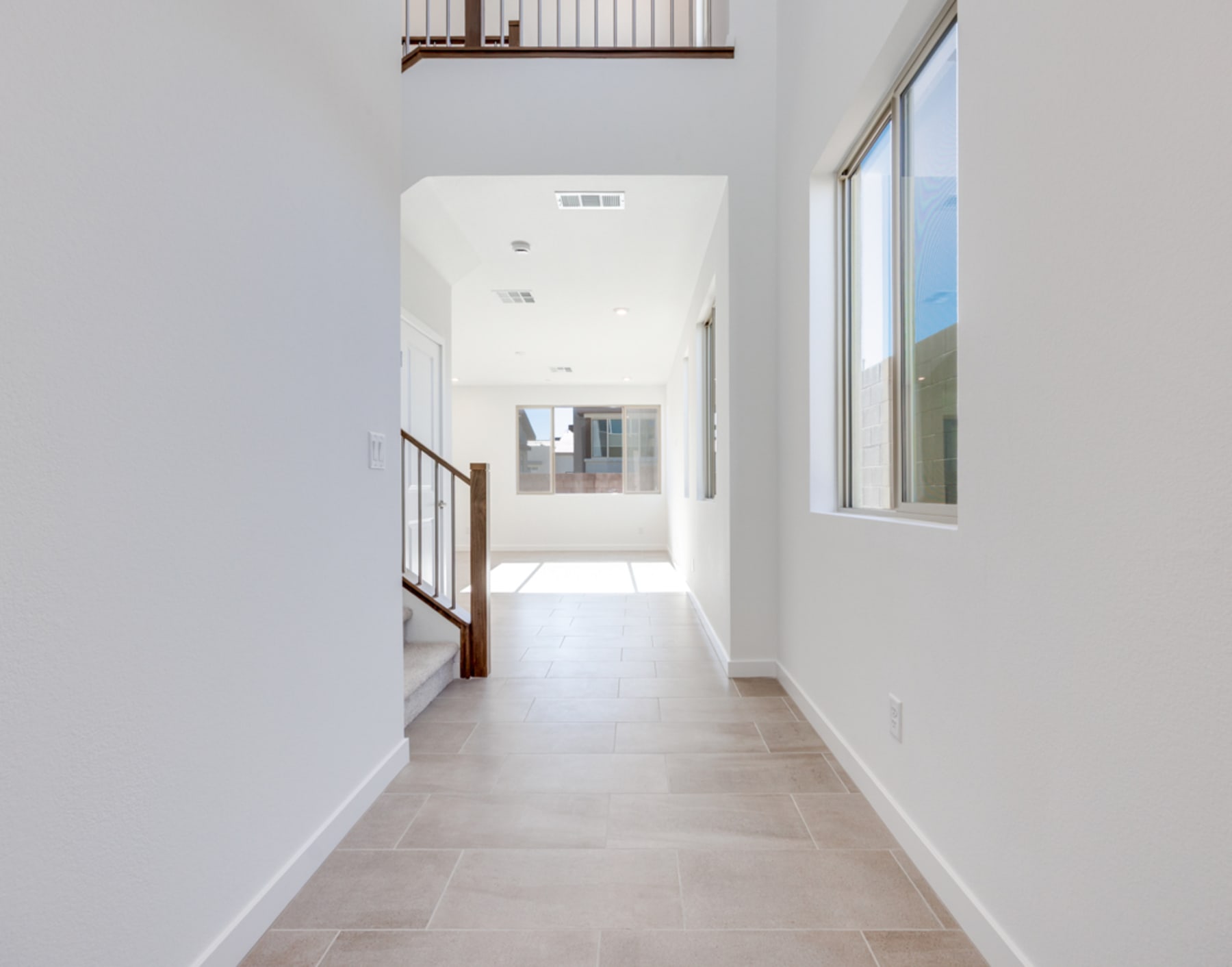 A bright, spacious hallway with white walls, a tiled floor, and a window at the end, providing natural light and a view of the outdoors.