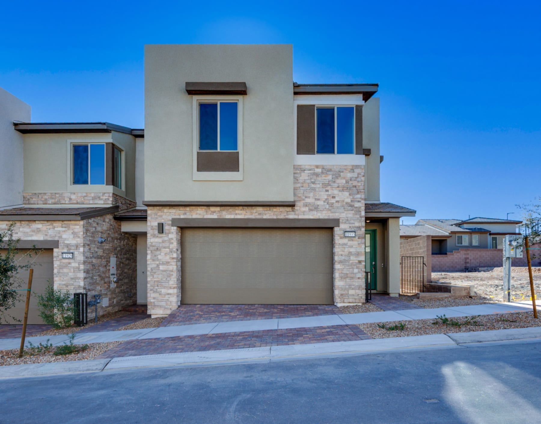 A modern two-story residential building with a stone facade, a garage door, and large windows against a clear blue sky.