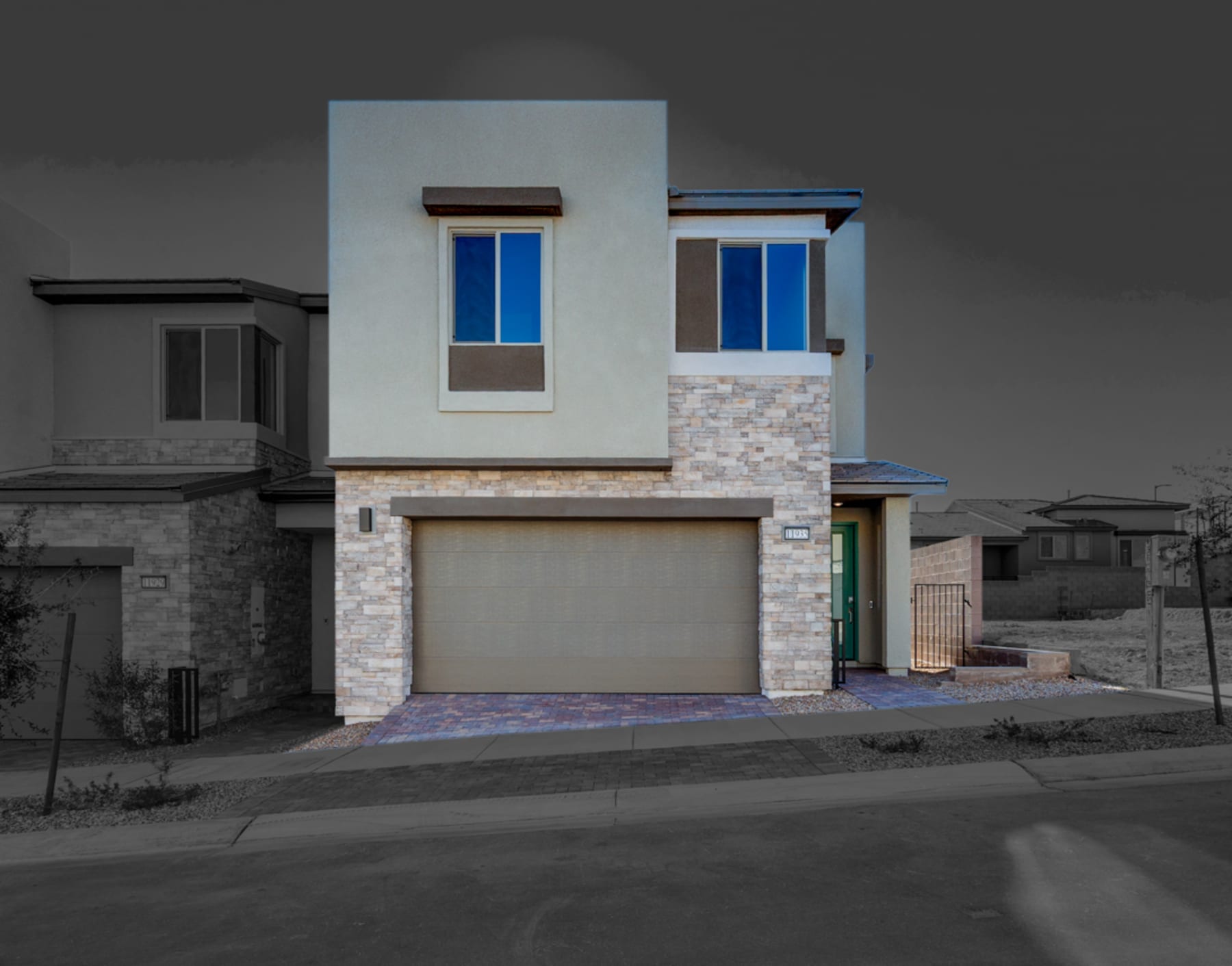 A modern two-story residential building with a stone facade, a garage door, and large windows that reflect the surrounding environment.