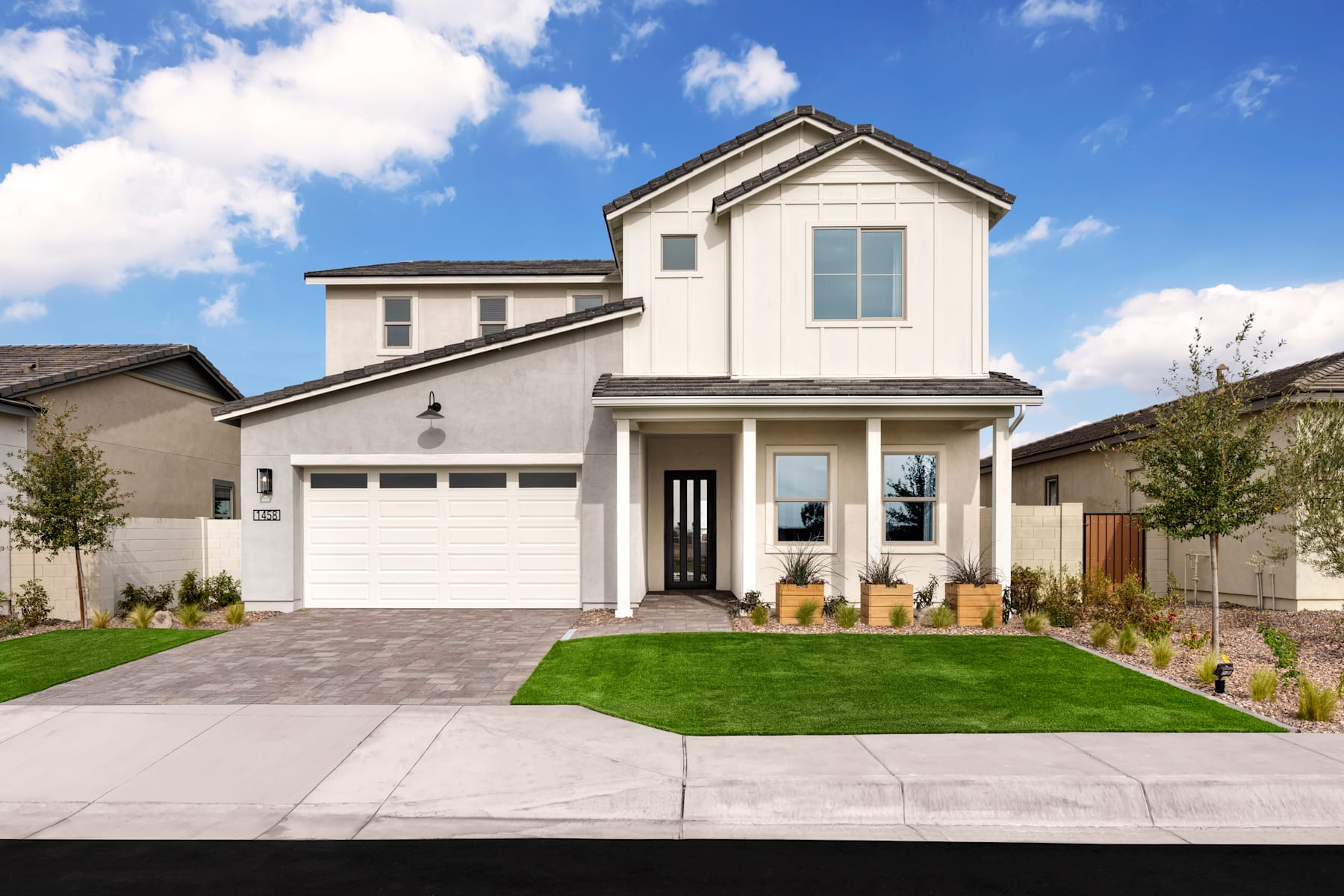 A two-story white house with a garage, surrounded by a well-manicured lawn and landscaping, set against a blue sky with fluffy white clouds.
