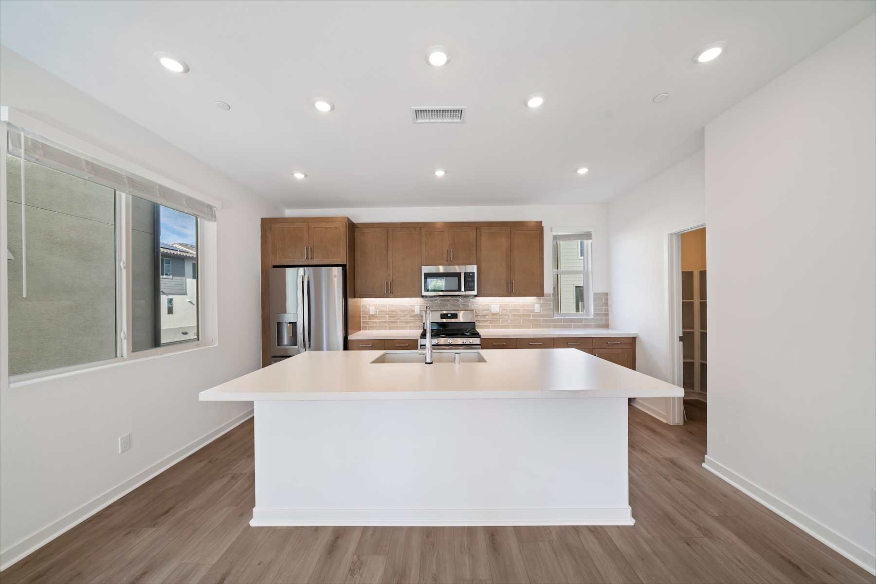 A modern, open-concept kitchen with white countertops, wooden cabinets, and stainless steel appliances, set against a bright, airy background.