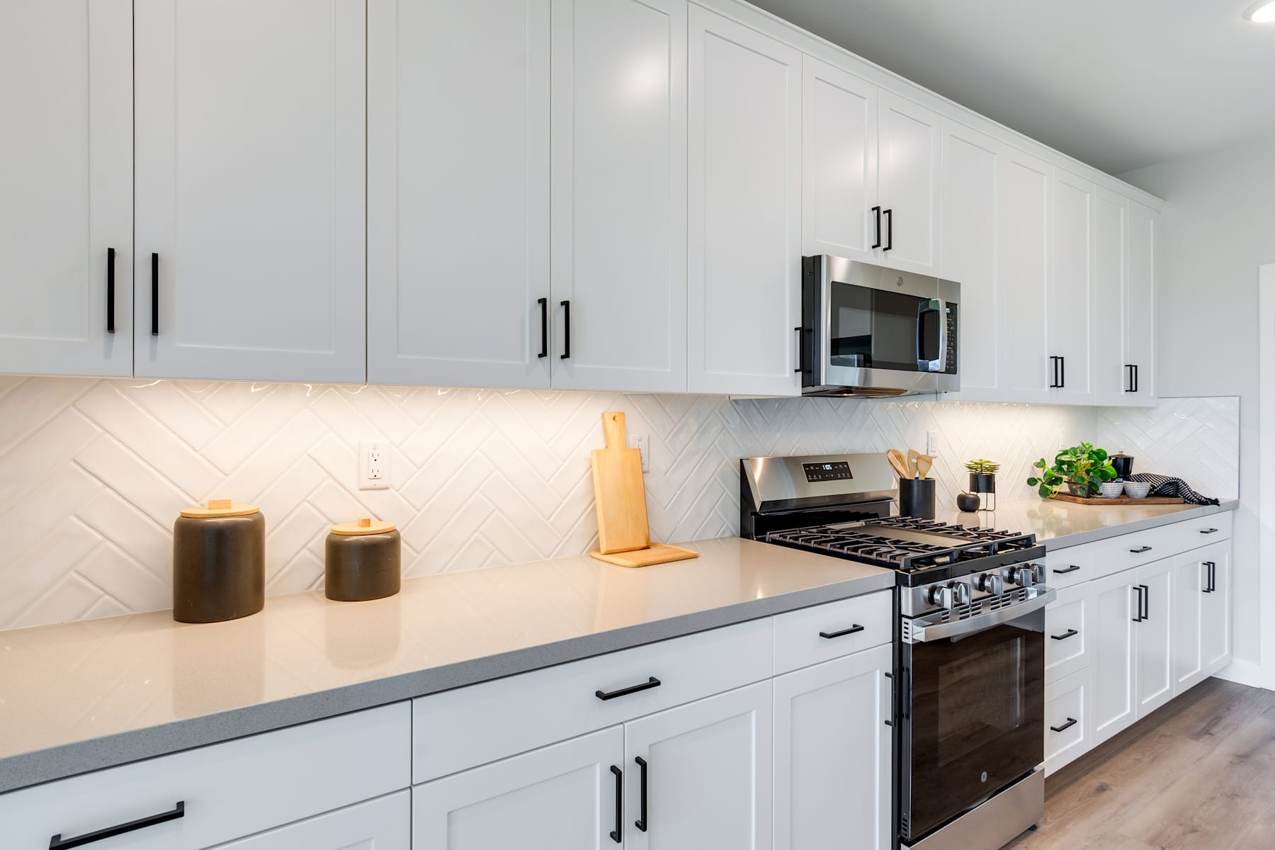 A modern, minimalist kitchen with white cabinets, a gas stove, and decorative elements on the countertop.