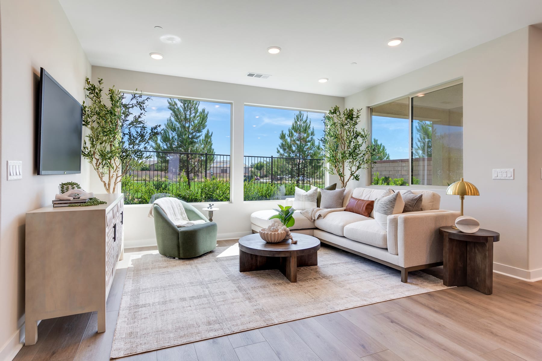 A cozy and inviting living room with large windows overlooking a lush, green outdoor landscape, featuring a comfortable sofa, armchair, and wooden coffee table.