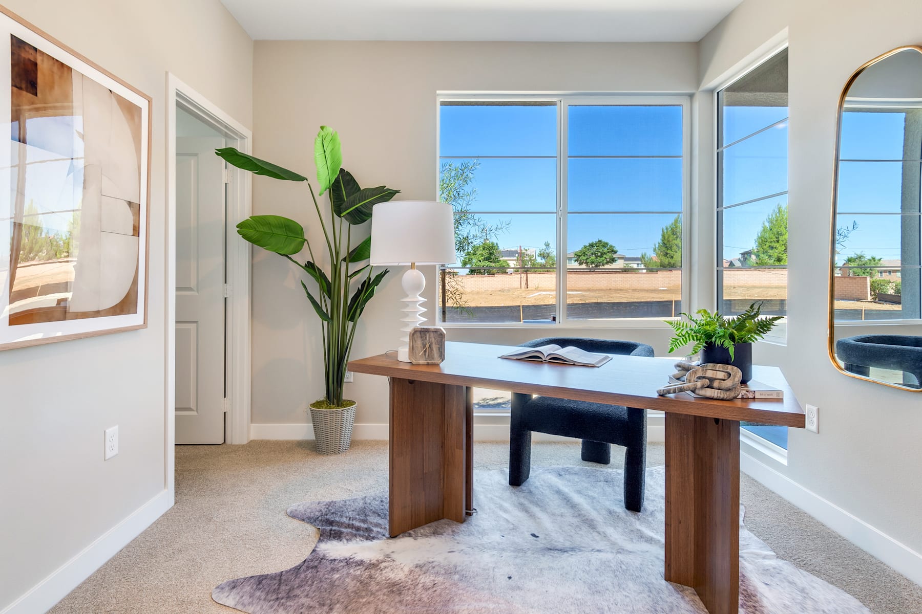 A bright and airy home office space with a wooden desk, potted plants, and large windows overlooking a scenic outdoor landscape.